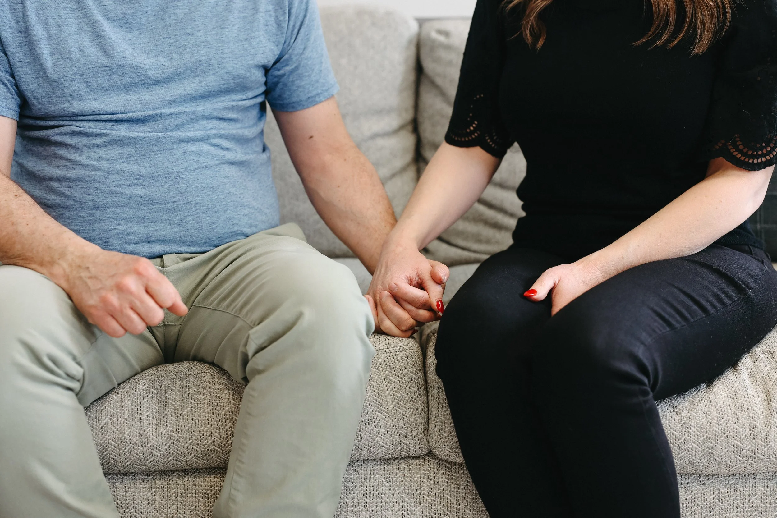 A man and woman sitting on a sofa, holding hands.
