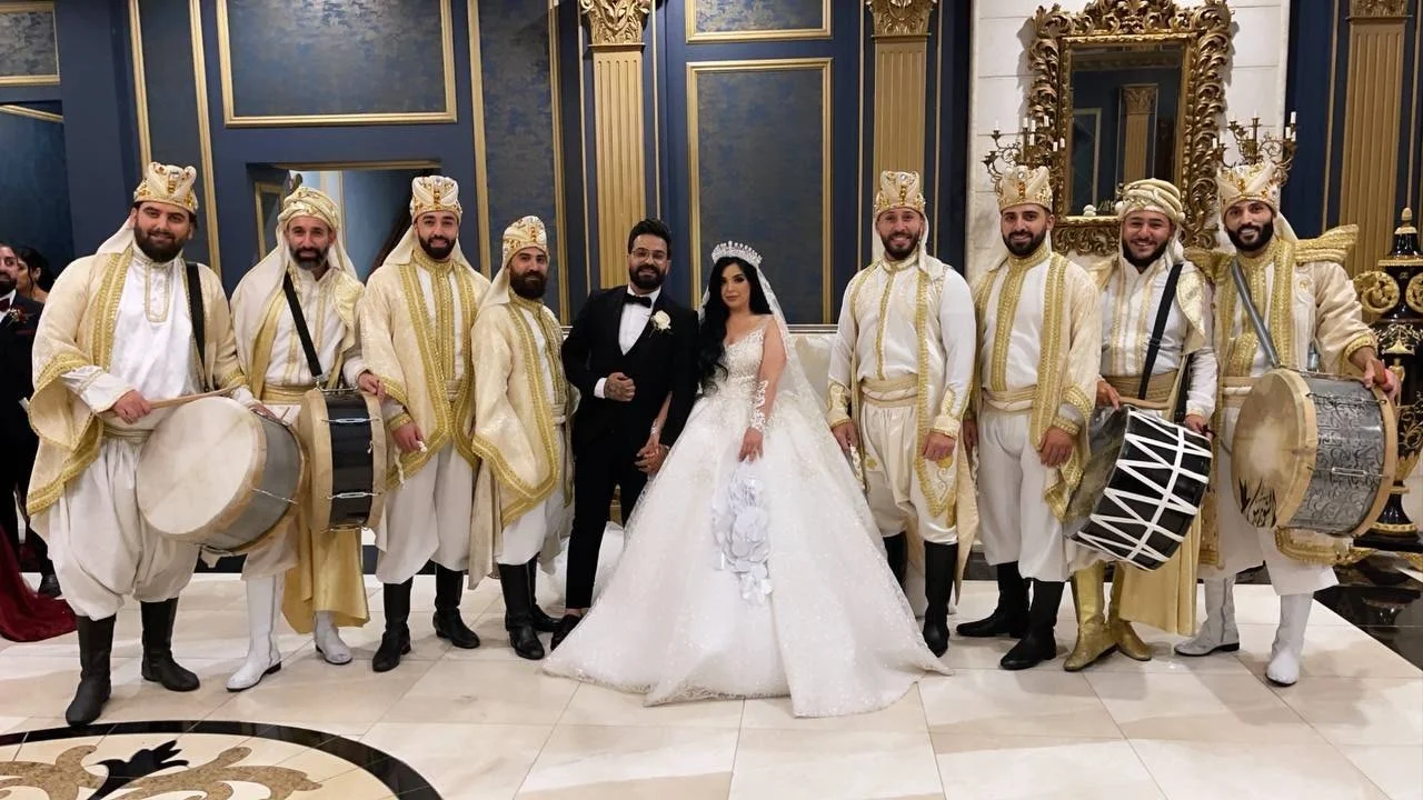 Bride and groom with a group in traditional attire and drums at a wedding.