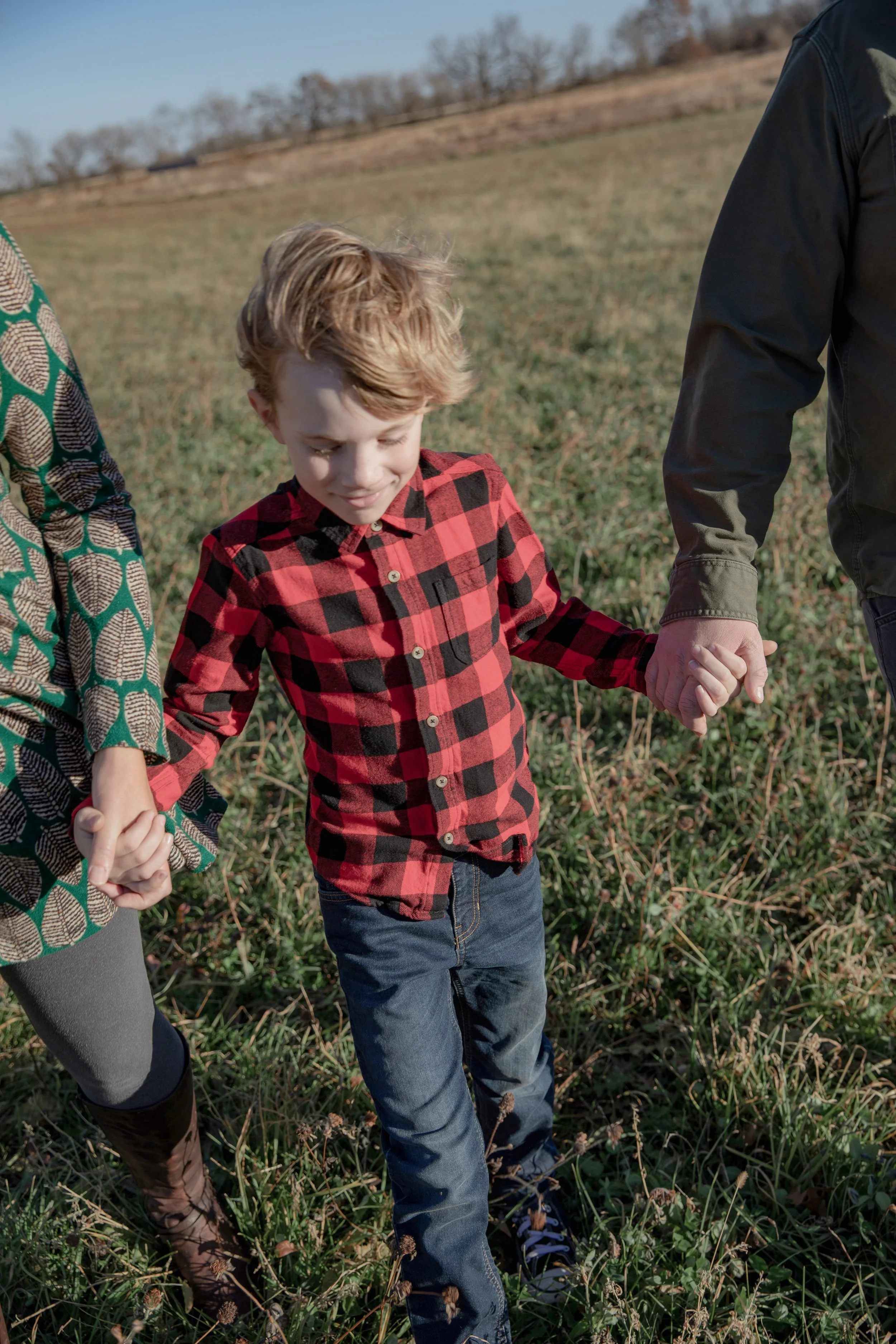 Picture of a boy smiling while holding his parents hands