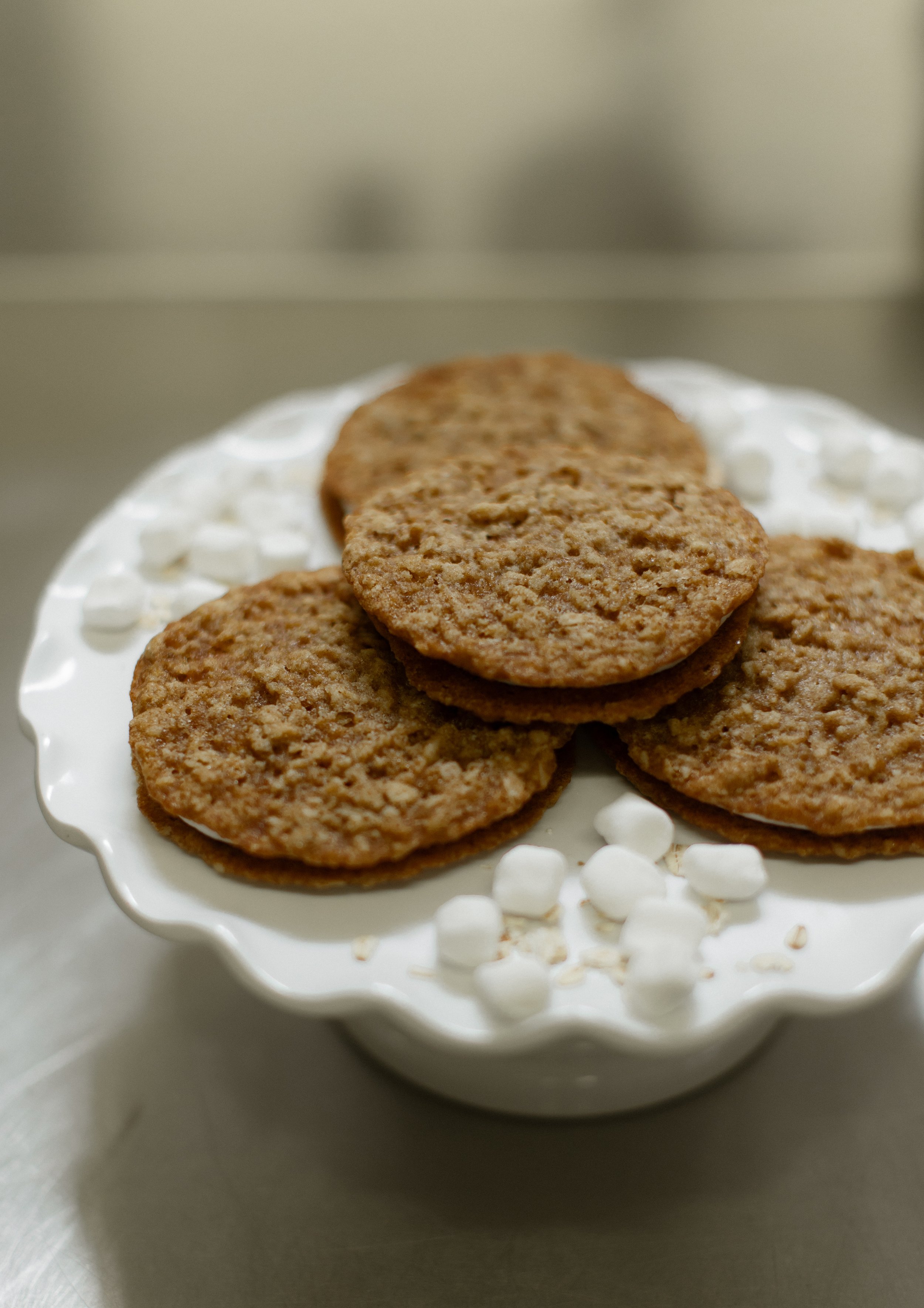 Oatmeal cookies on a white cake stand with mini marshmallows.