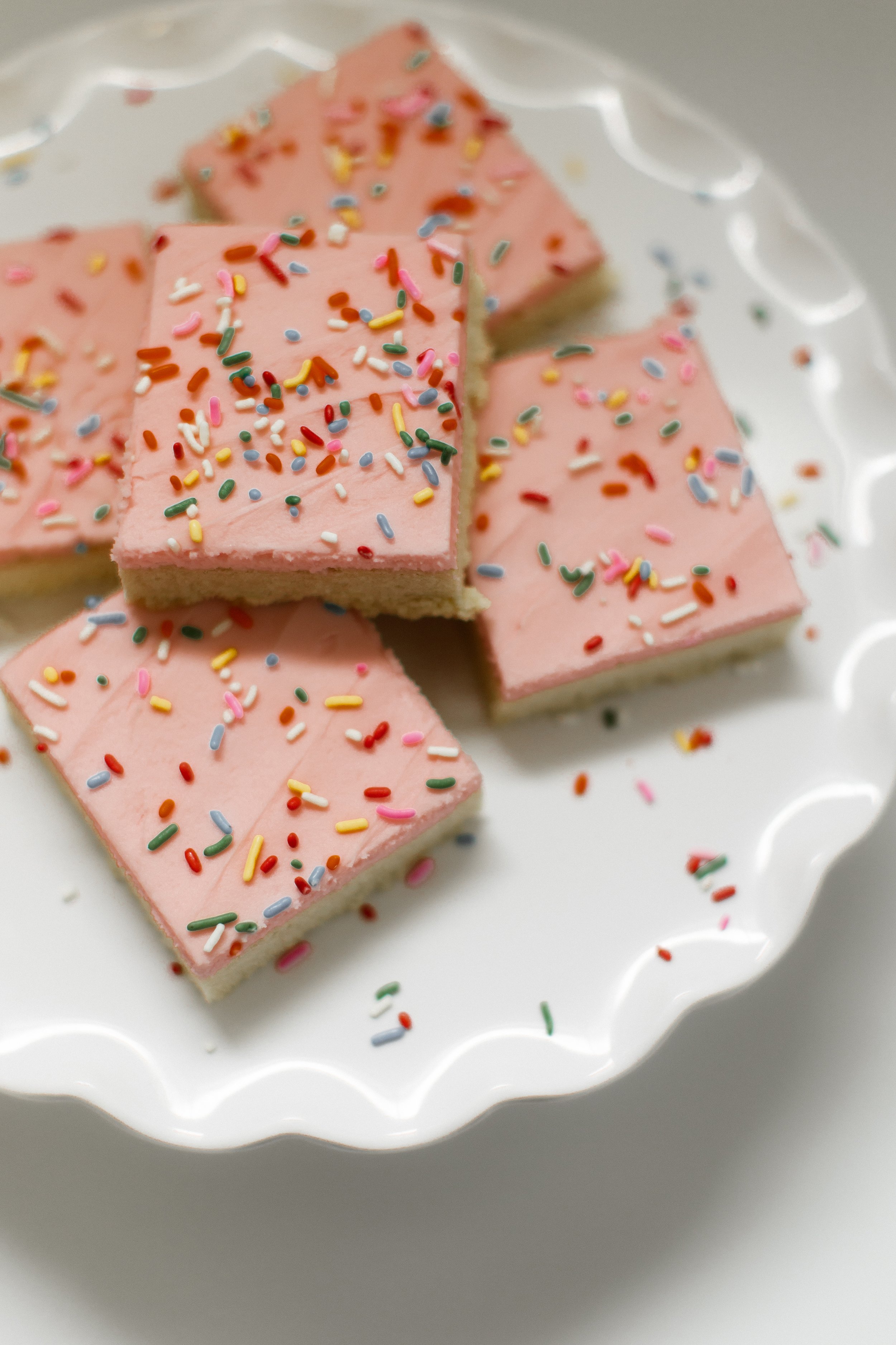 Pink frosted sugar cookie bars with rainbow sprinkles on a white plate.