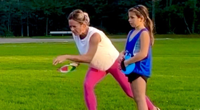 Coach Caroline and young girl playing on a grassy field with a ball, outdoors during daytime for GLOW Lacrosse in Massachusettes