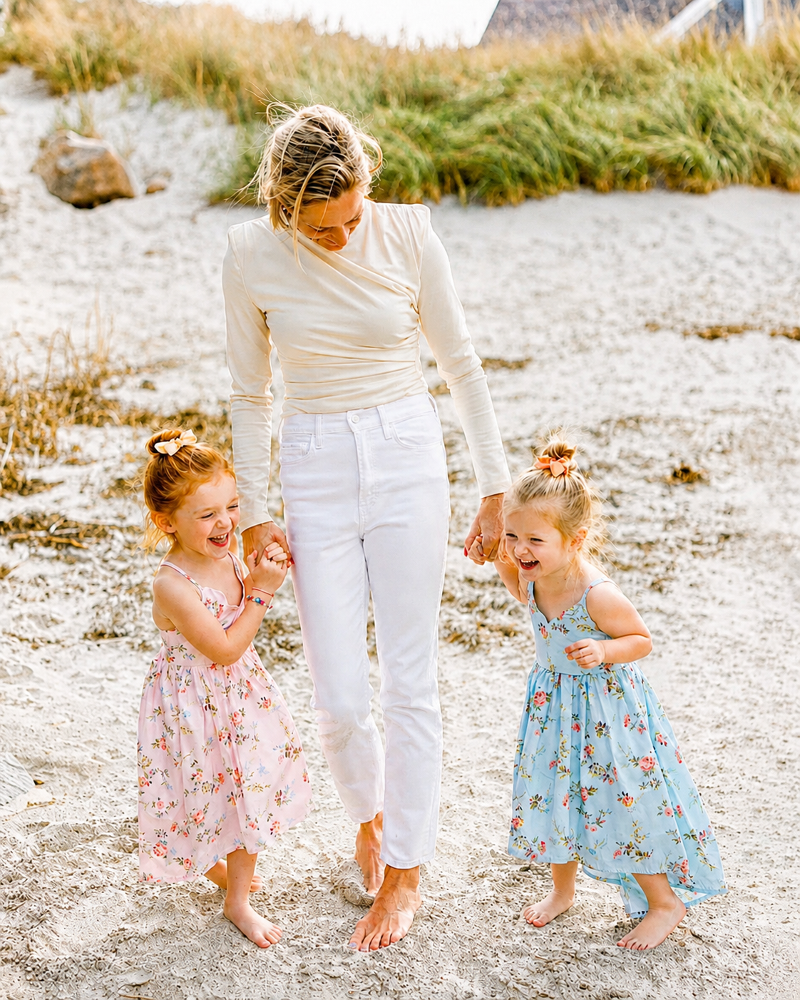 A woman walking on the beach holding hands with two young girls, all smiling and laughing.