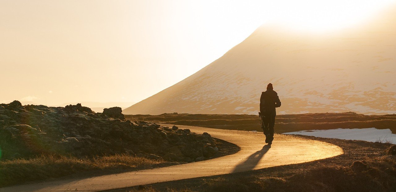A person walking on a winding dirt path in a mountainous landscape at sunrise or sunset.