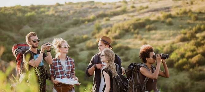 Group of five hikers outdoors with backpacks, two women and three men, one woman with binoculars.