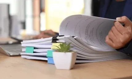 Office desk with a laptop, smartphone, glasses, documents, and a potted plant