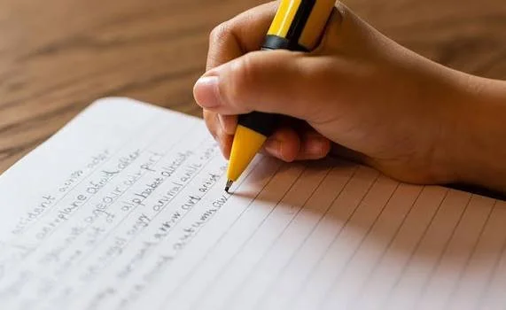 A person writing in a notebook with a yellow pen.
