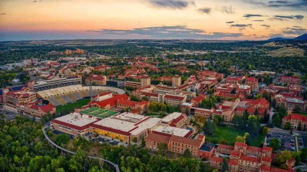Aerial view of a college campus with red brick buildings, sports fields, and surrounding greenery at sunset.