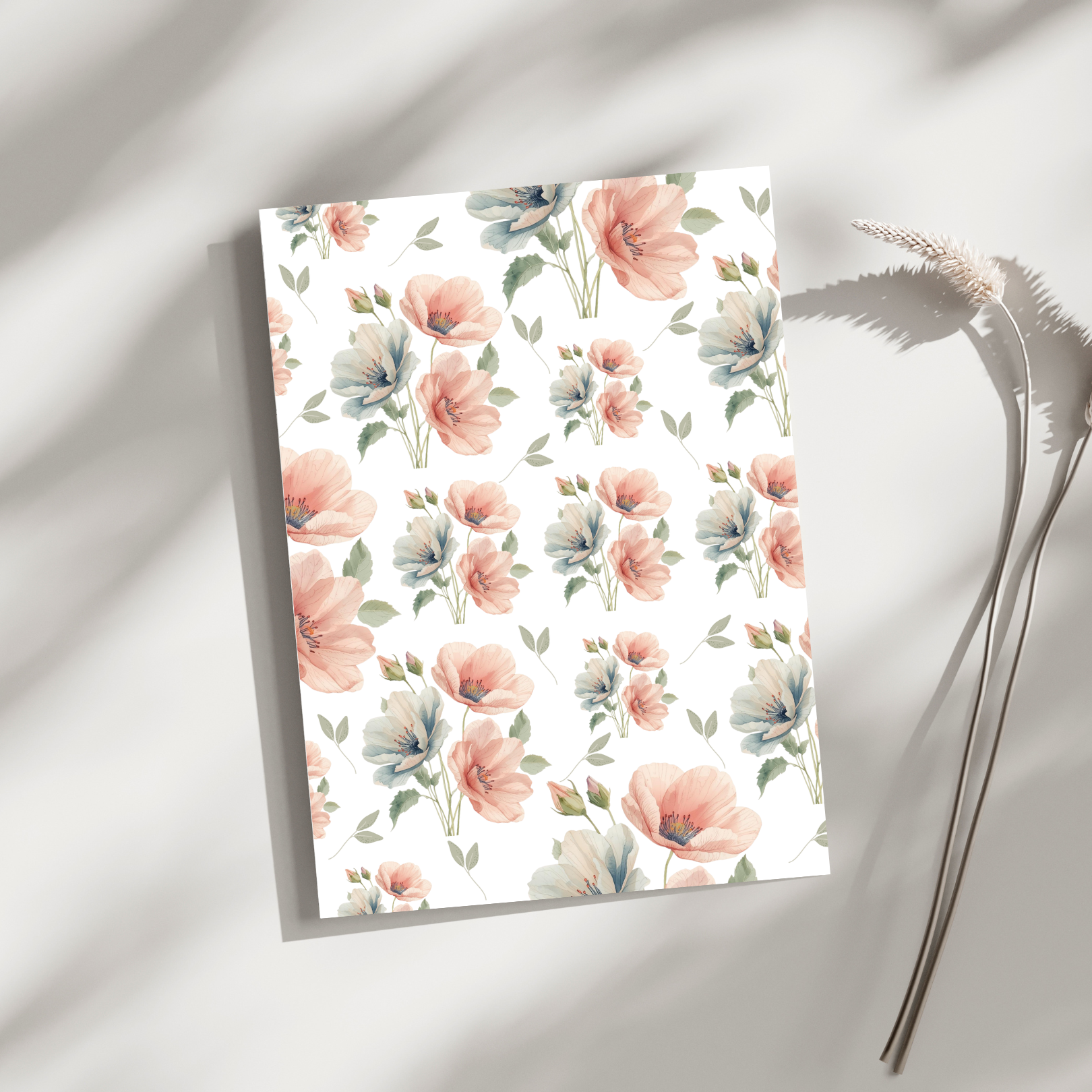 A floral-patterned paper with pink and light blue flowers and green leaves, placed on a white surface with soft shadows, accompanied by a dried flower stem.