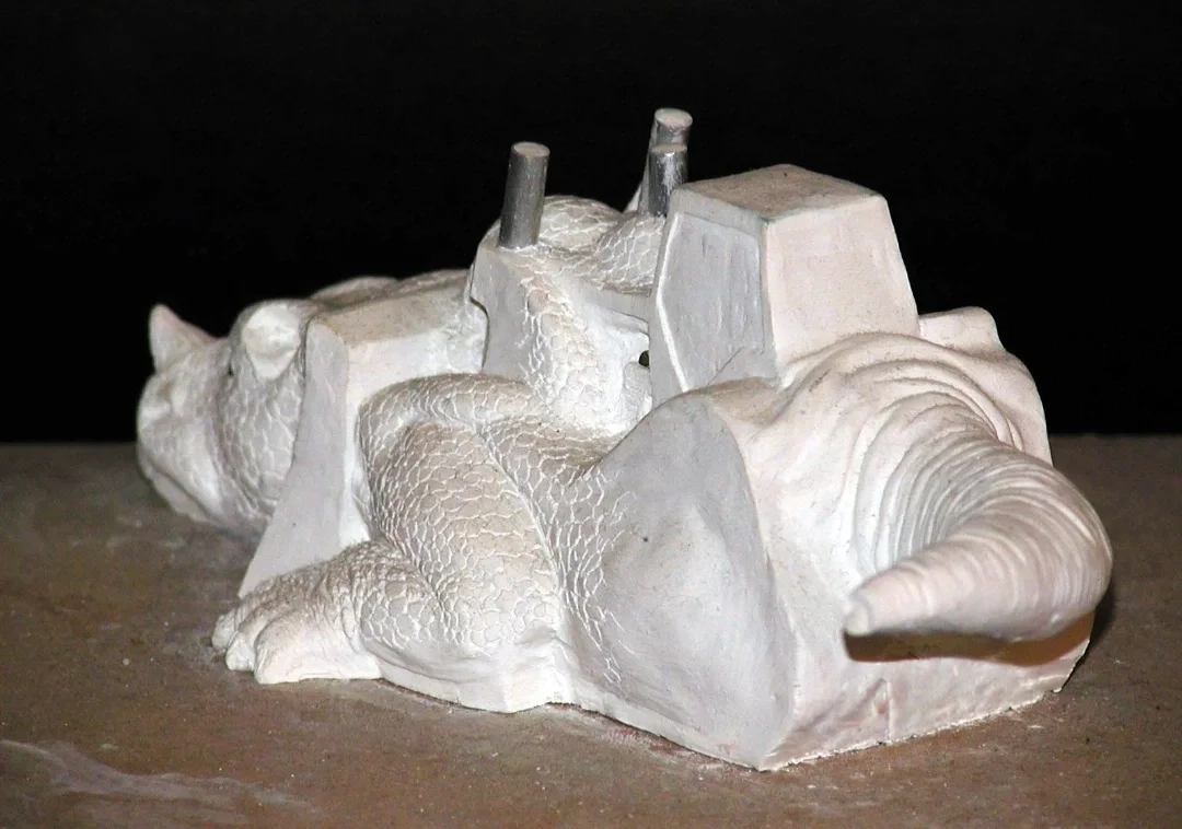 White sculpture of a lizard with a truck on its back against a black background.