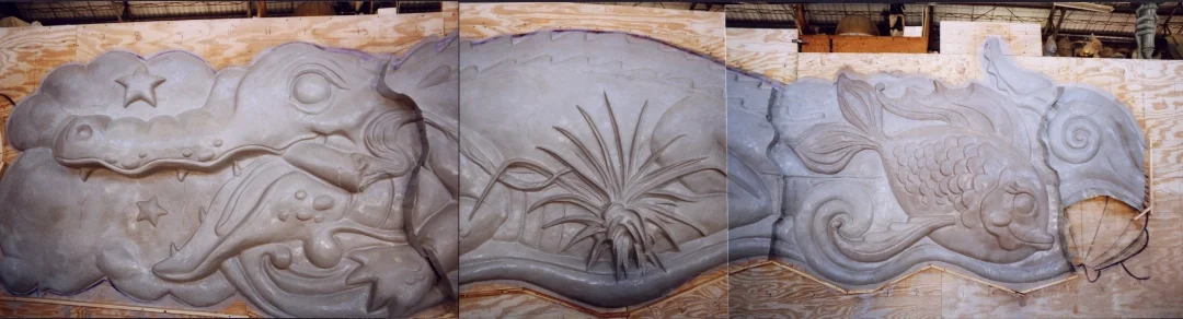 A carved stone relief featuring a crocodile with stars on its back, a plant in the center, and a fish with a swirl on its side.
