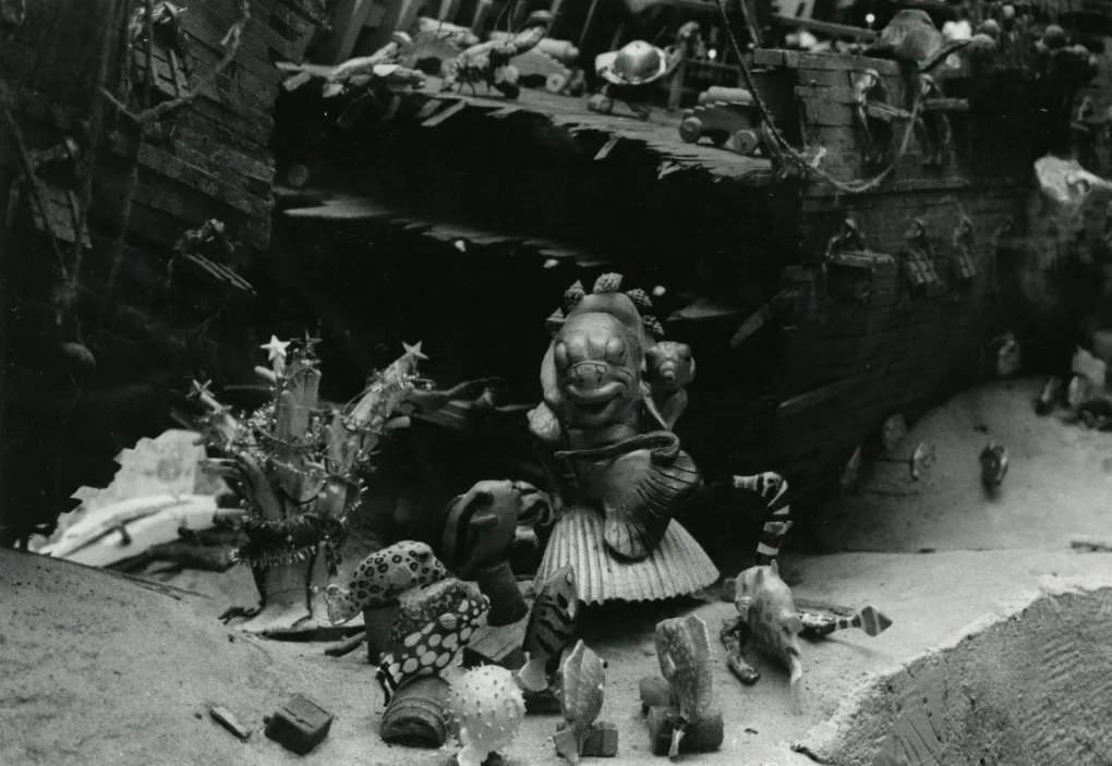 A collection of toy figurines and objects arranged in front of a model ship in a diorama setting.