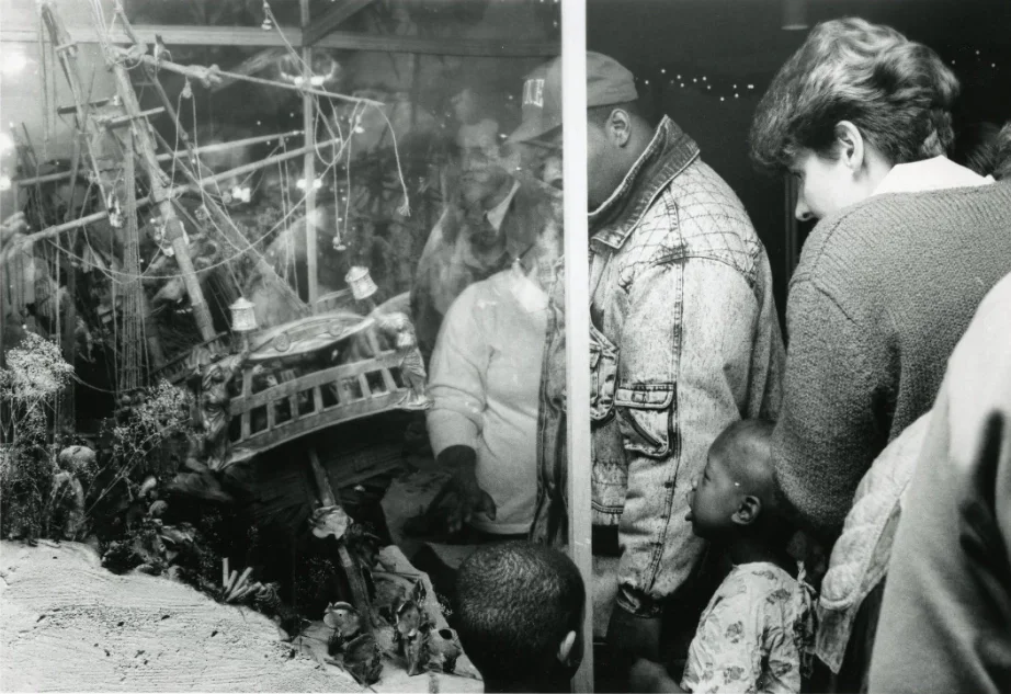 Group of people observing a model ship display behind glass at a museum or exhibit.