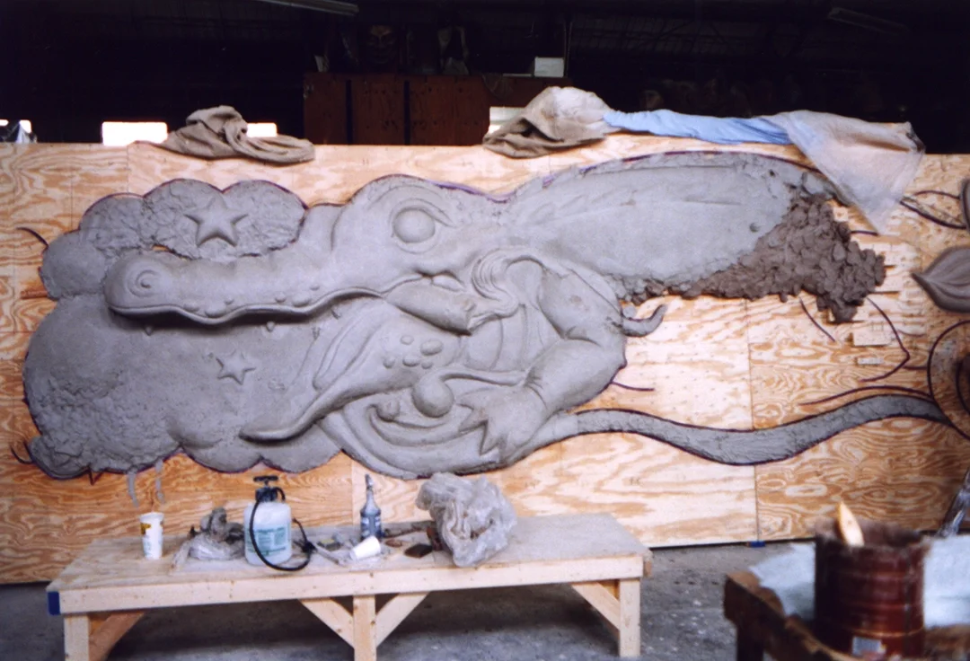 Sand sculpture of a lizard with a cloud in the background.