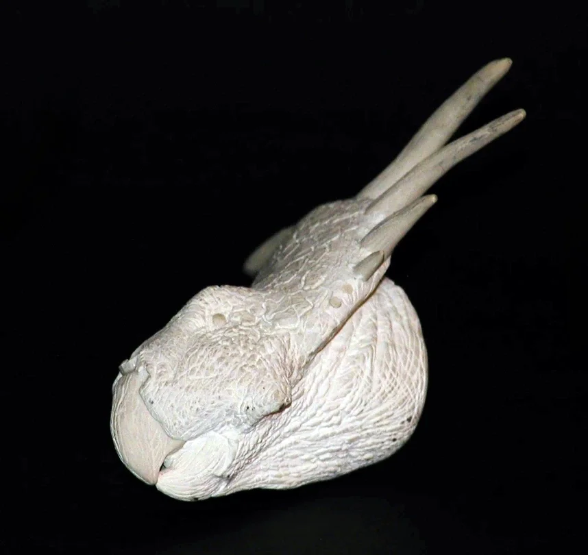A white ceramic sculpture of a bird with elongated, tapering feathers against a black background.