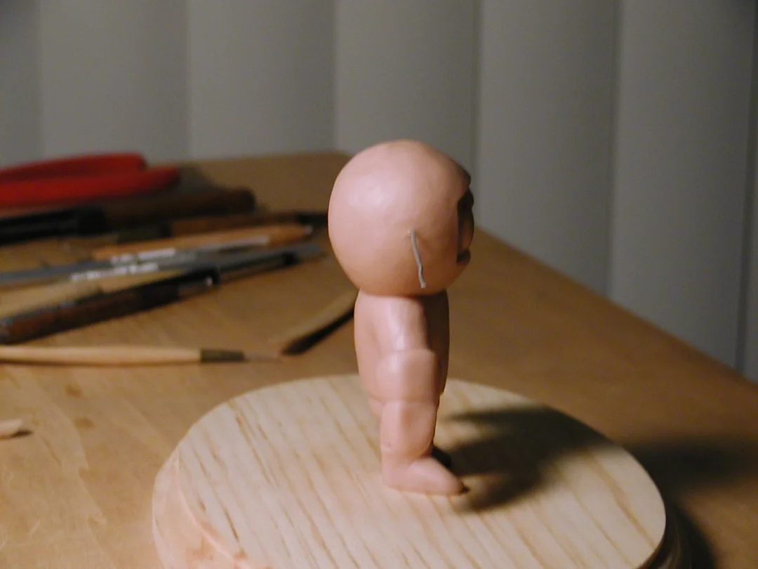 A small figurine with a human body and a round head that is larger than the body, standing on a wooden surface with various tools in the background.