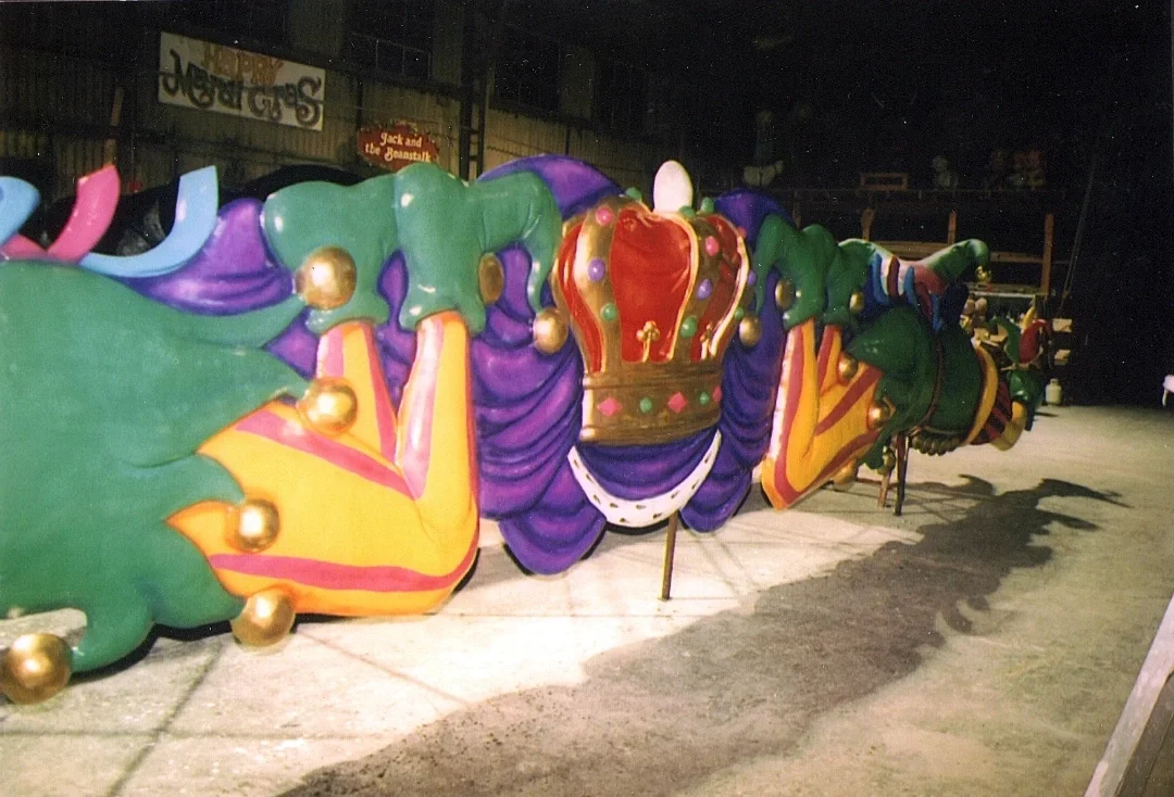 Colorful carnival float designed as a dragon with a crown, purple and green body, and gold accents, set up outdoors at night.