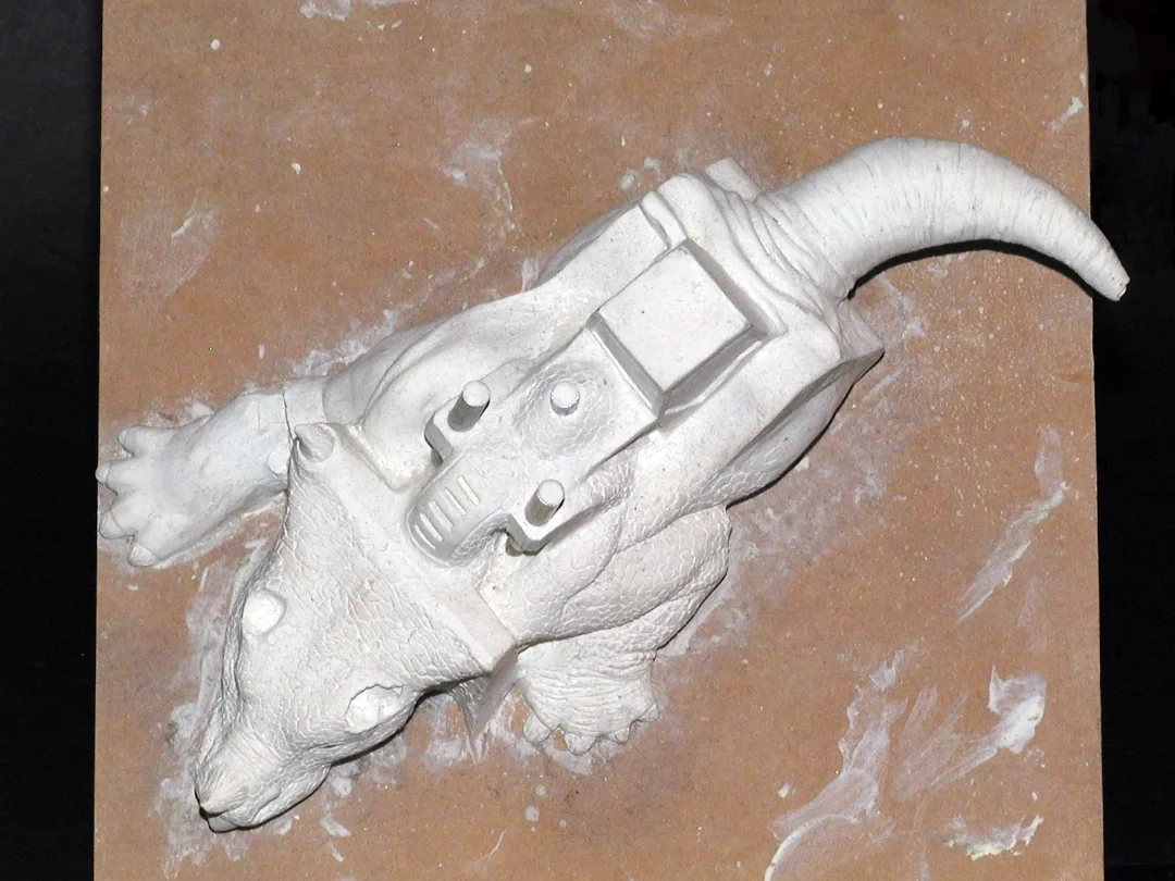 White sculpture of a rat with a sci-fi gun on its back, lying on a brown work surface.