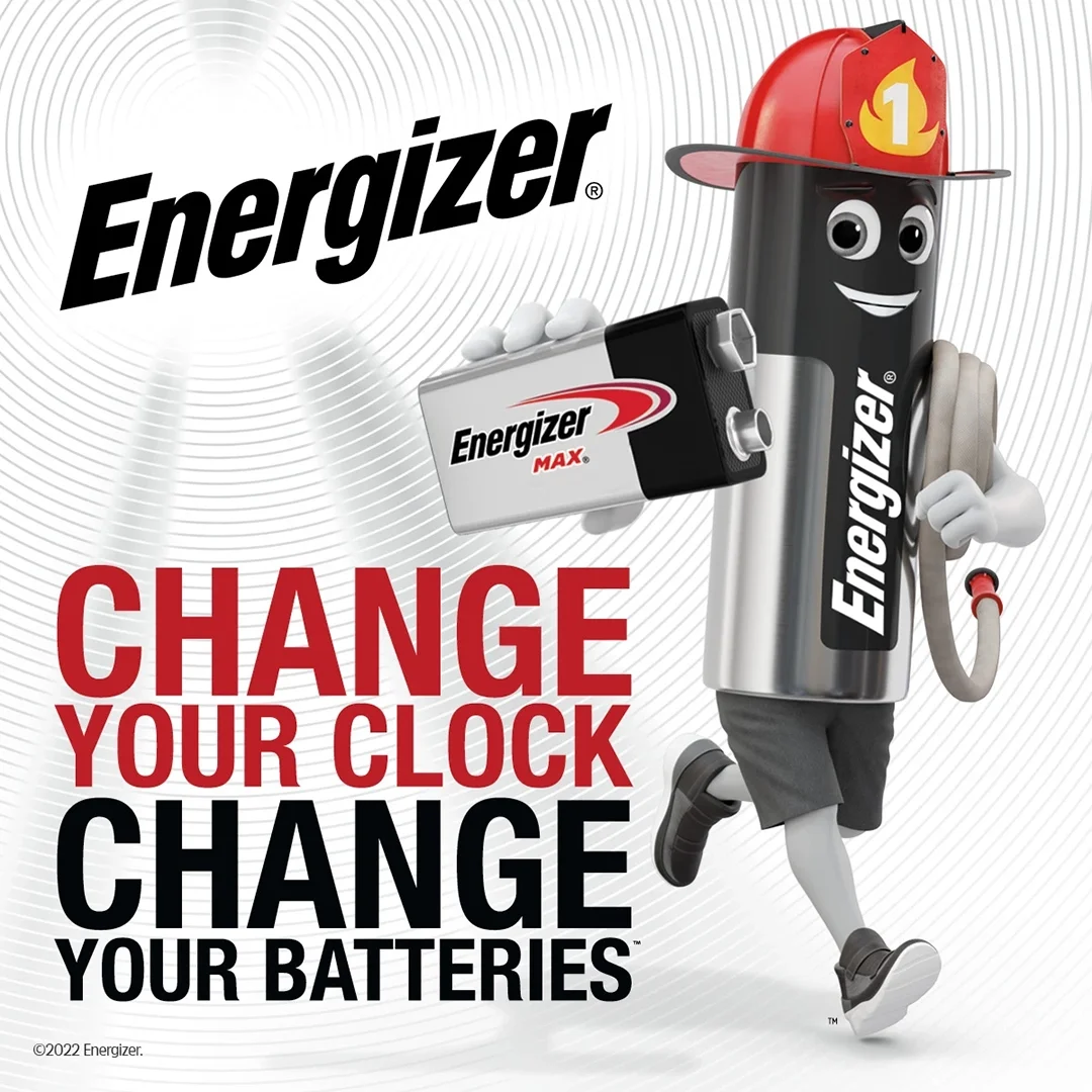 Energizer advertisement featuring a cartoon battery character wearing a firefighter helmet and holding a battery, with text that says 'Change Your Clock, Change Your Batteries'.