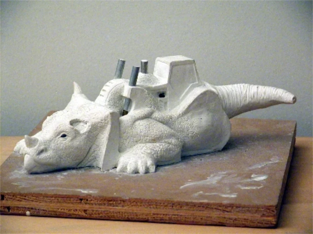 A sculpture of a sleeping dragon with a mechanical saddle and a small structure on its back, made of white material on a wooden base.