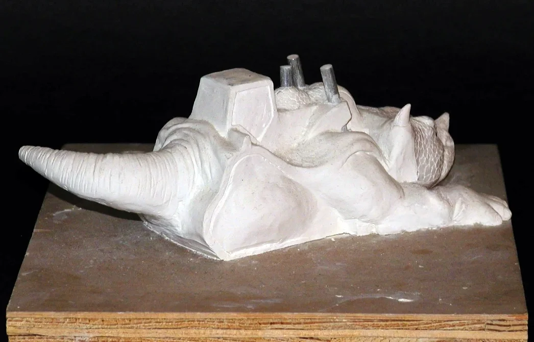 Clay sculpture of a dinosaur skull with a large horn on the nose and a small one above the eye, and a textured skull pattern.