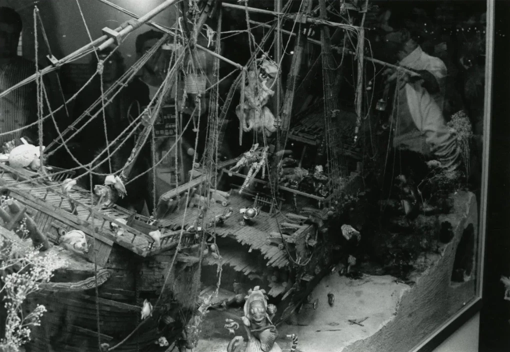 A detailed model of a pirate ship with masts, rigging, and deck, displayed in a glass case at a museum.