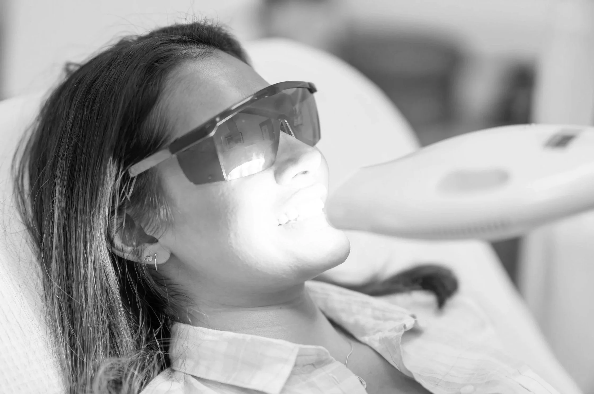 A woman lying on a hospital bed while receiving laser dental treatment with protective eyewear.