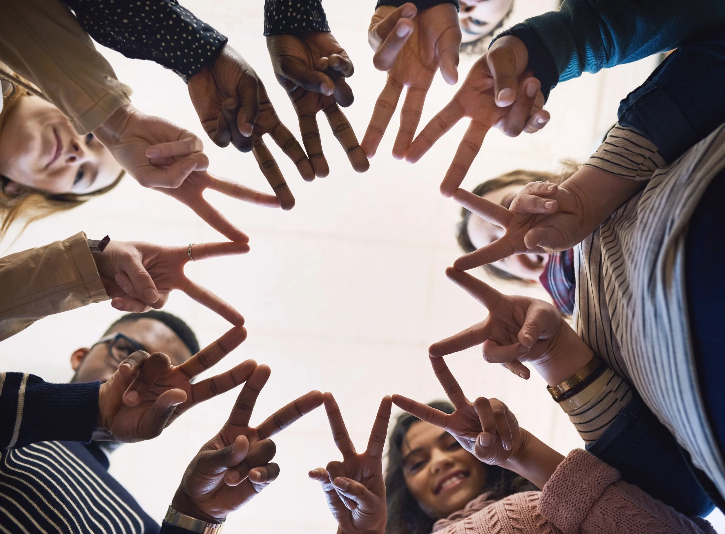 Group of diverse people forming a circle with their fingers, seen from below.