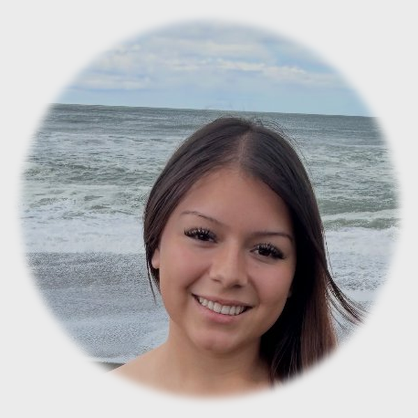 Lady with long dark hair, black outfit, bright smile, beach background
