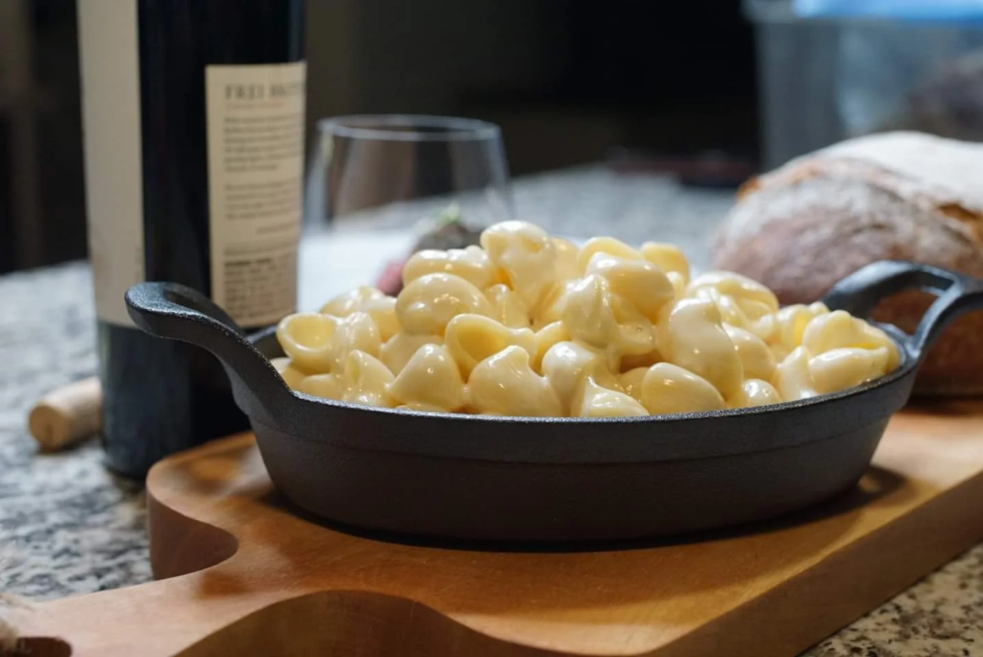 Creamy macaroni and cheese in a black cast iron skillet placed on a wooden cutting board, on a kitchen countertop.