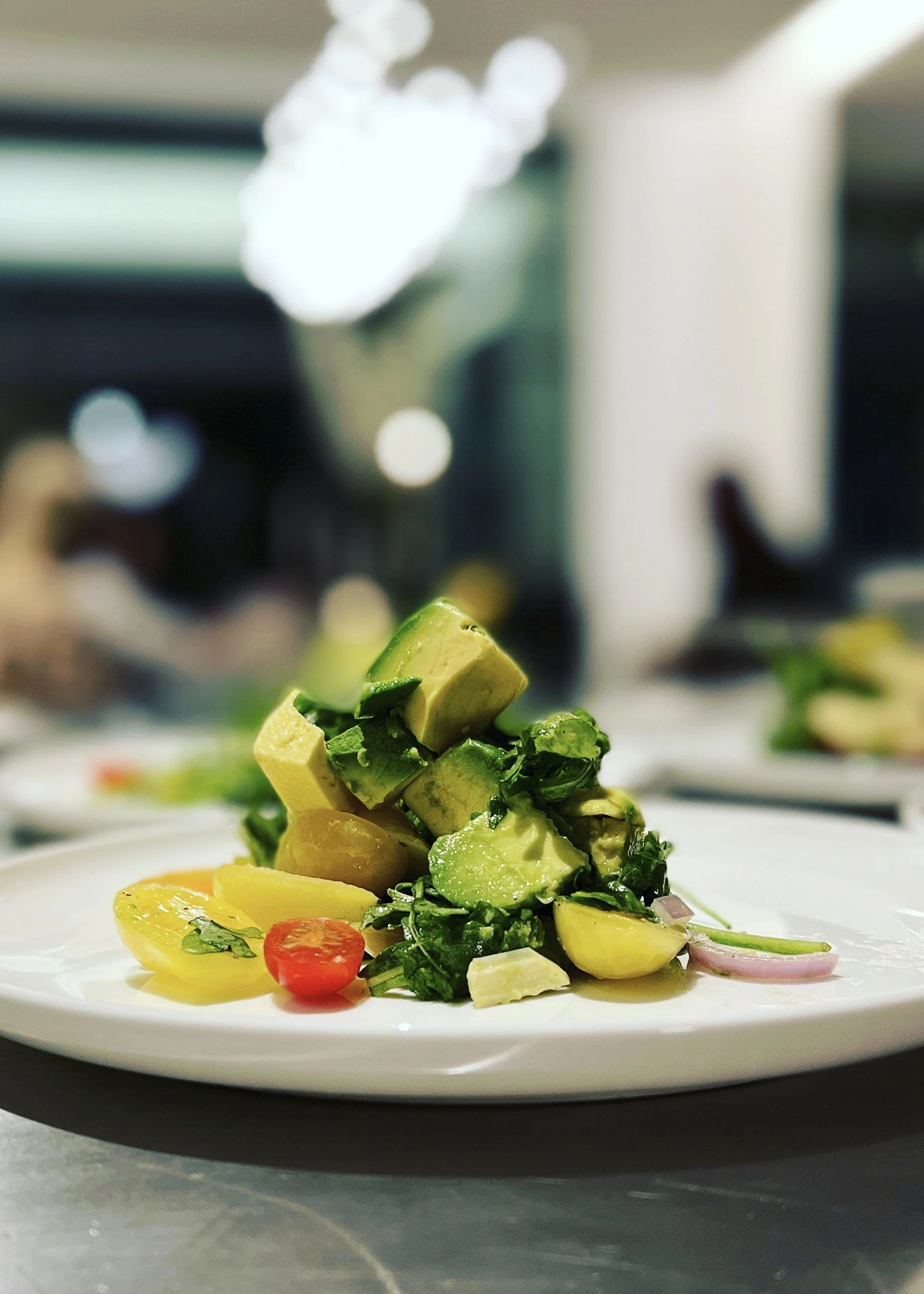A plate of chopped avocado, cherry tomatoes, and sliced red onions, with a blurred kitchen background.
