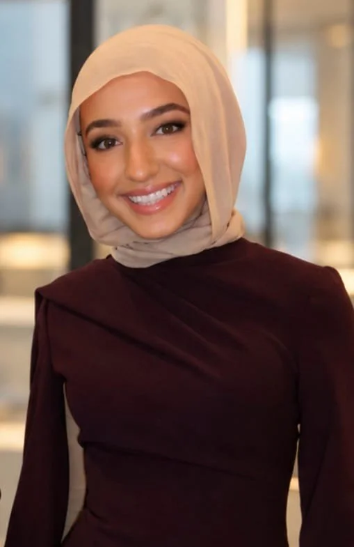 Smiling woman wearing a beige hijab and burgundy long-sleeve top