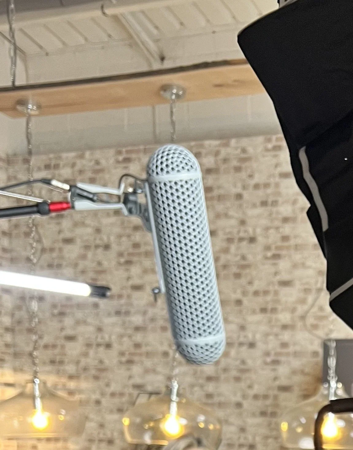 A microphone mounted on a stand hanging from a wooden ceiling beam in a room with a brick wall background.