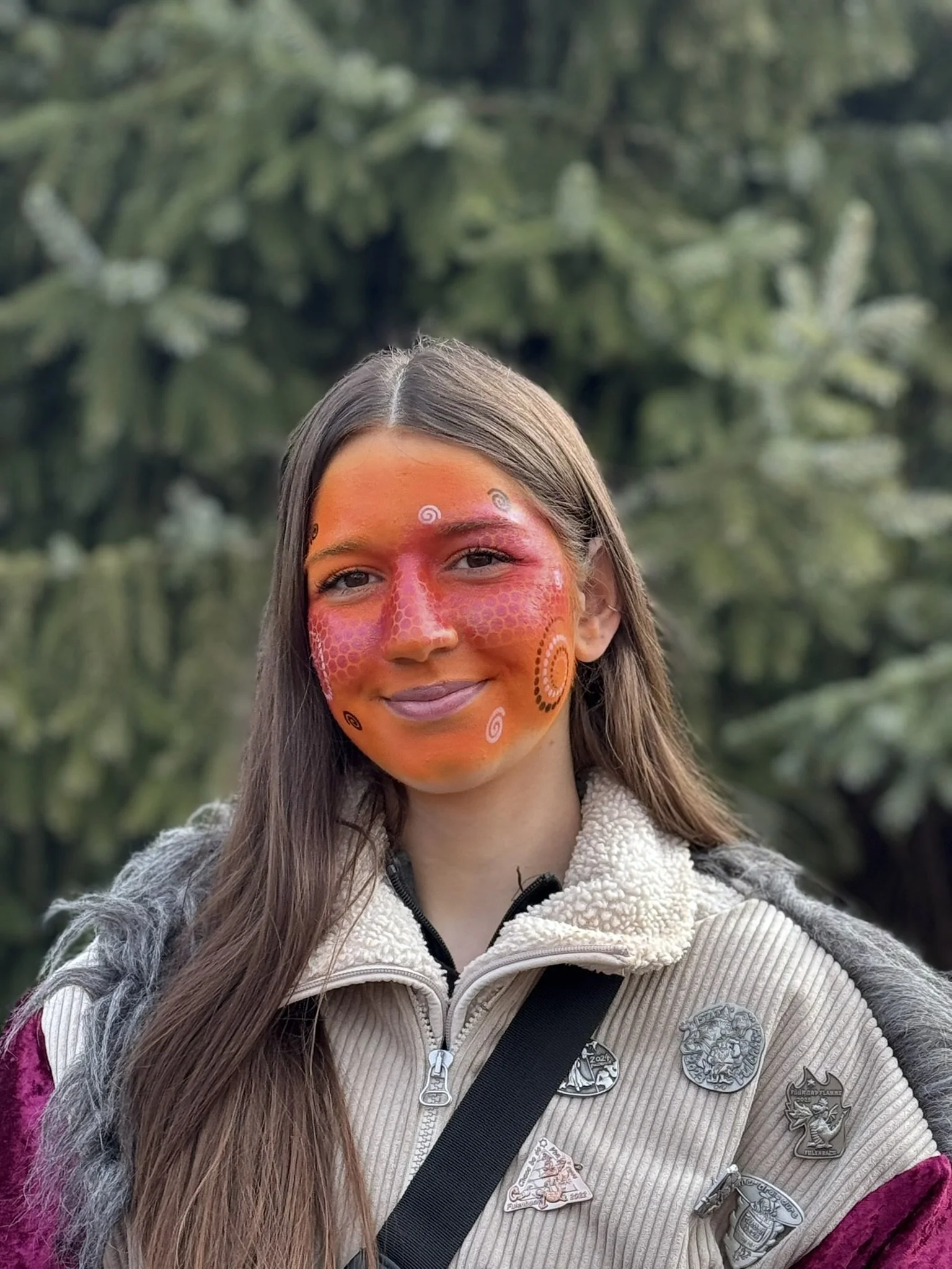 Junge Frau mit Buntkörperbemalung auf Gesicht im Freien, umgeben von Bäumen.