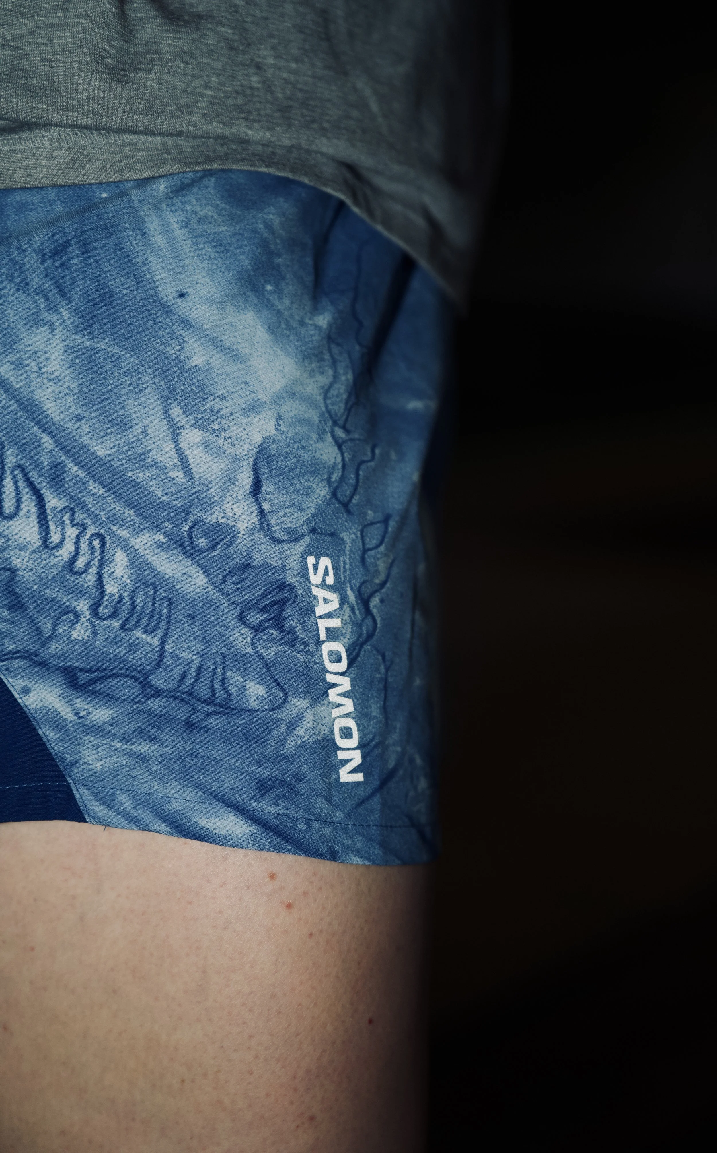 Close-up of a person's upper thigh wearing a blue patterned fabric with the word 'SALON' visible, with skin showing below.