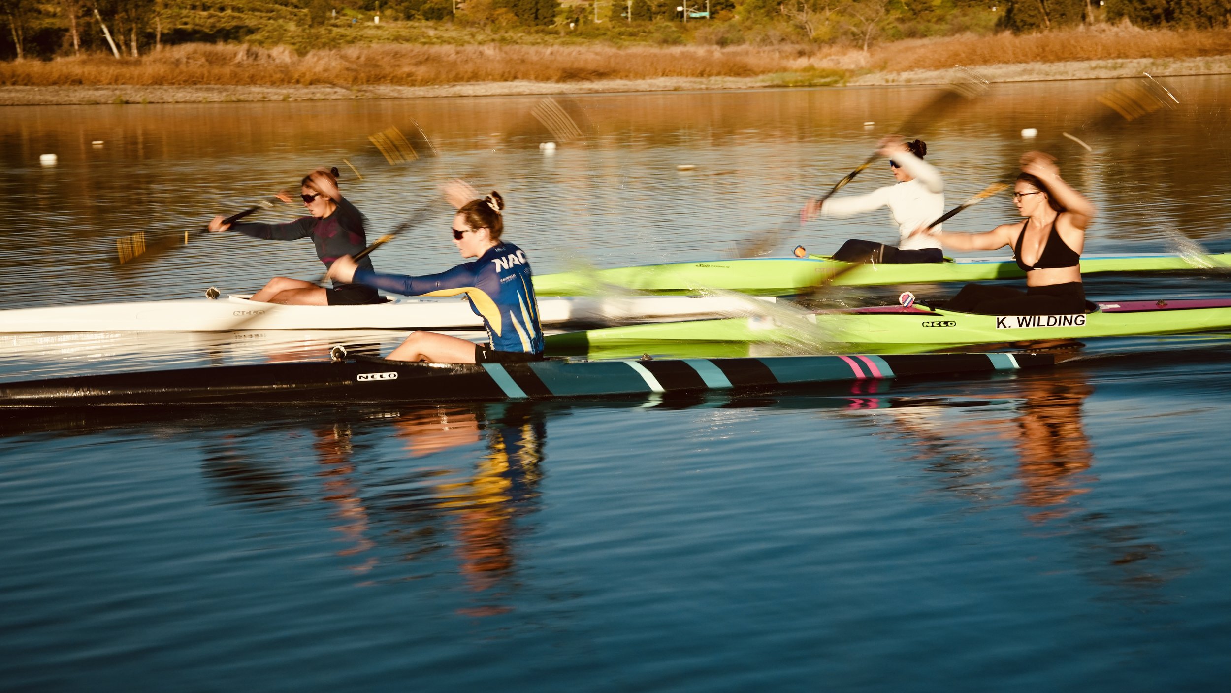 Four women kayaking on a calm river during sunset.