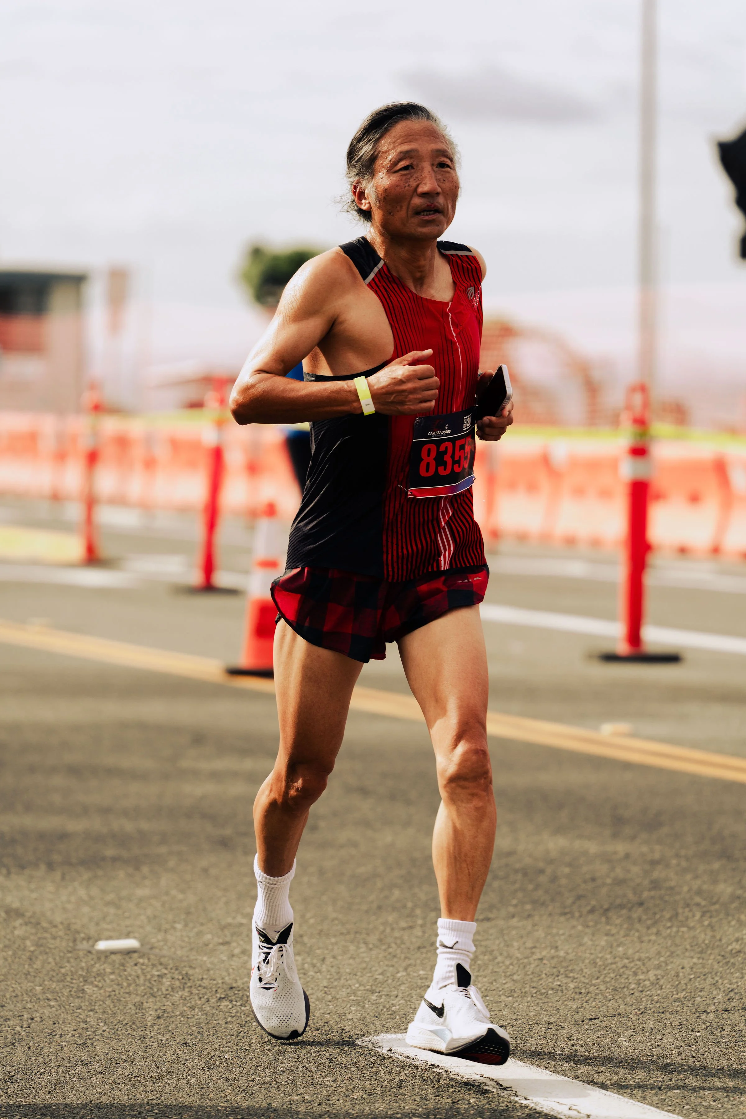 A male runner in athletic gear running on a track during daytime, with orange traffic cones and blurred background.