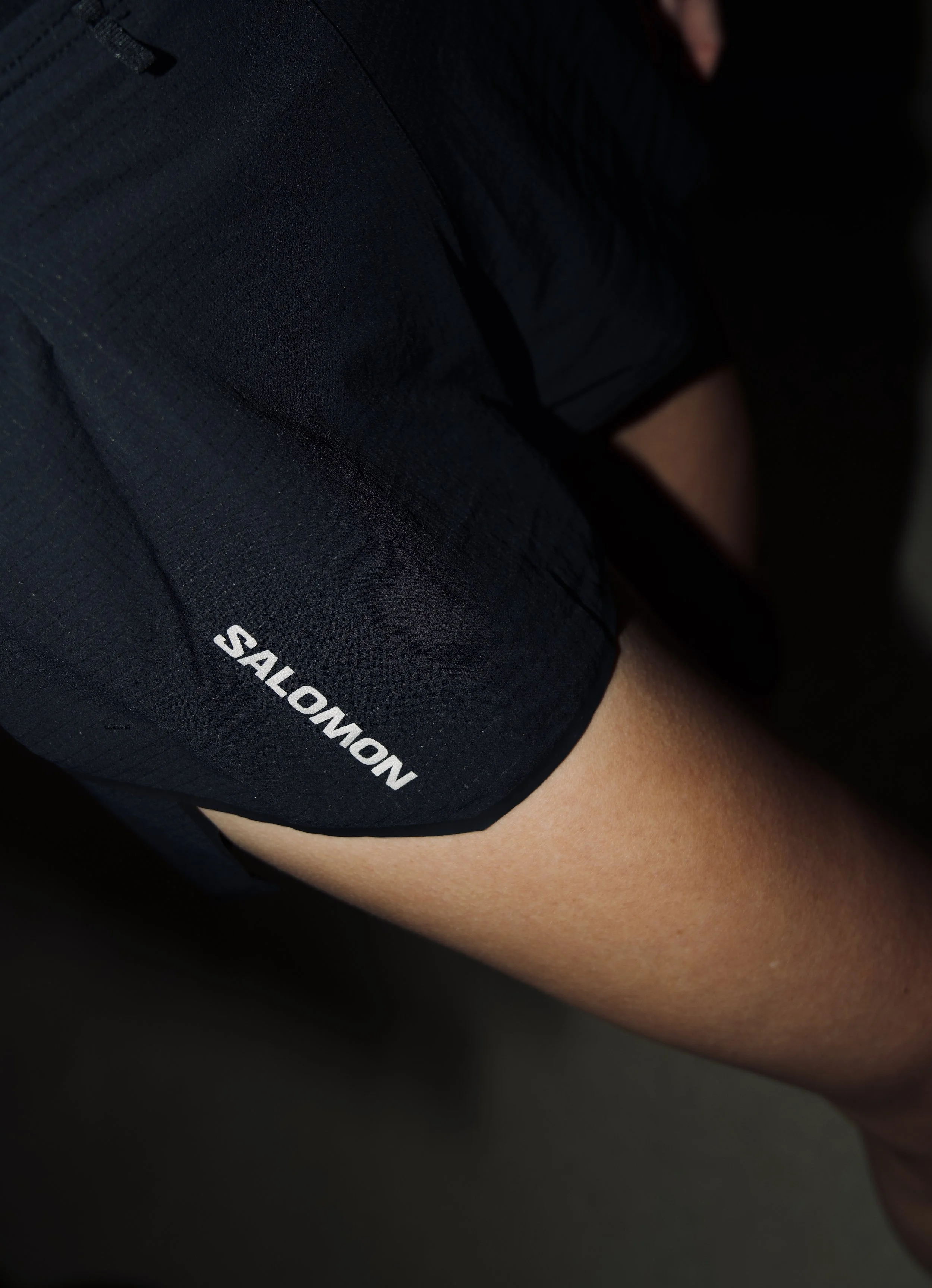 Close-up of a person wearing black athletic shorts with the word 'NOMAD SALOMON' printed on the side, showing part of their bare leg.