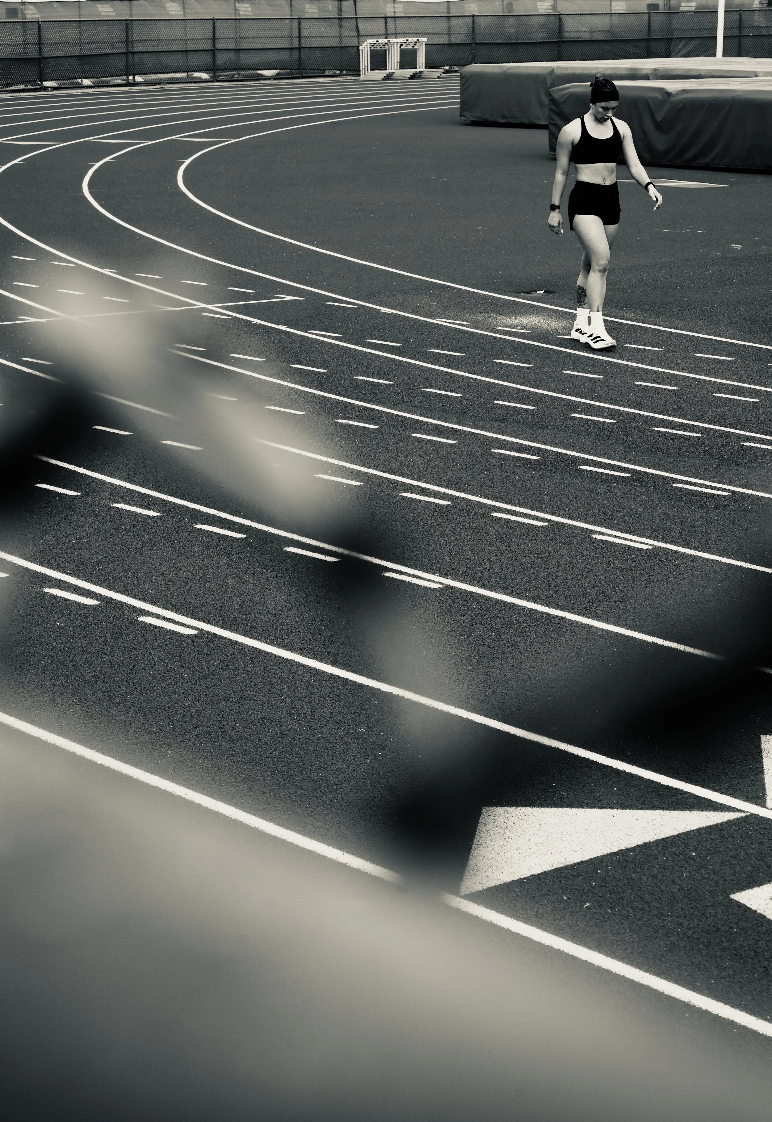 A female athlete walking on an outdoor running track, dressed in black sportswear and white sneakers.