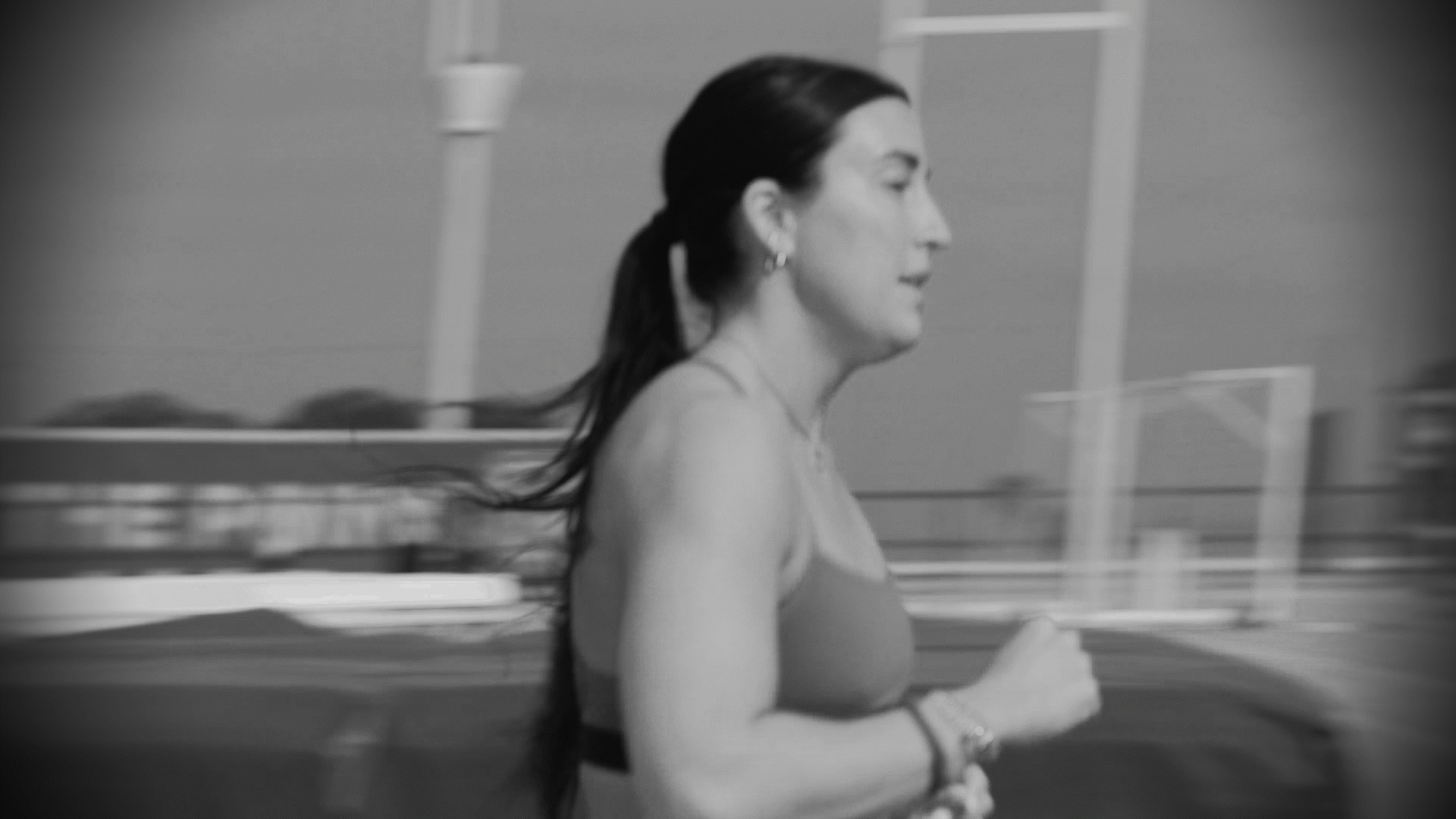 Black and white image of a woman running with her hair tied back, outdoors at a park or similar setting.