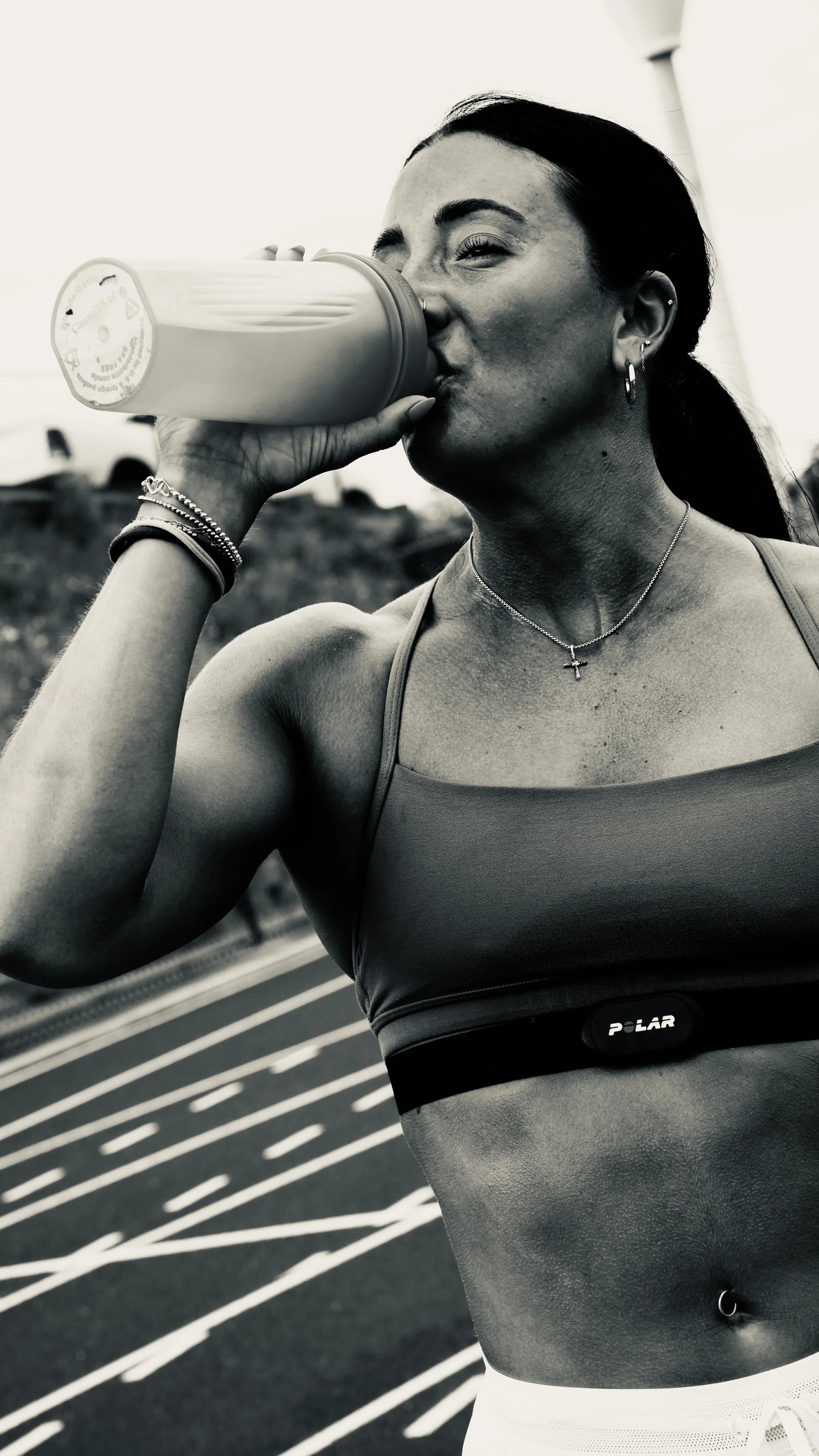 A woman drinking from a water bottle while exercising outdoors on a track.