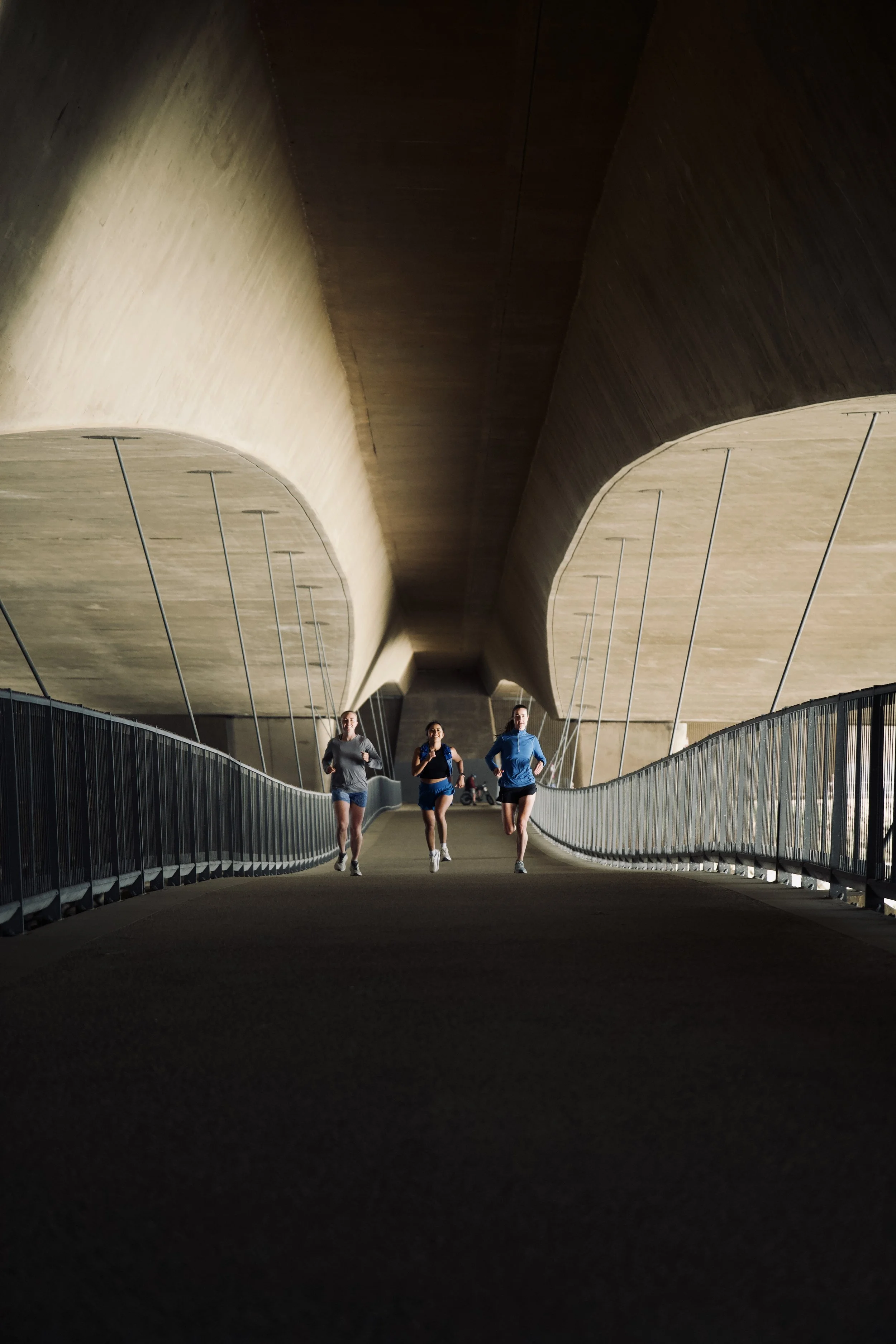 Three people jogging in a tunnel with curved walls and ceiling, illuminated from behind.