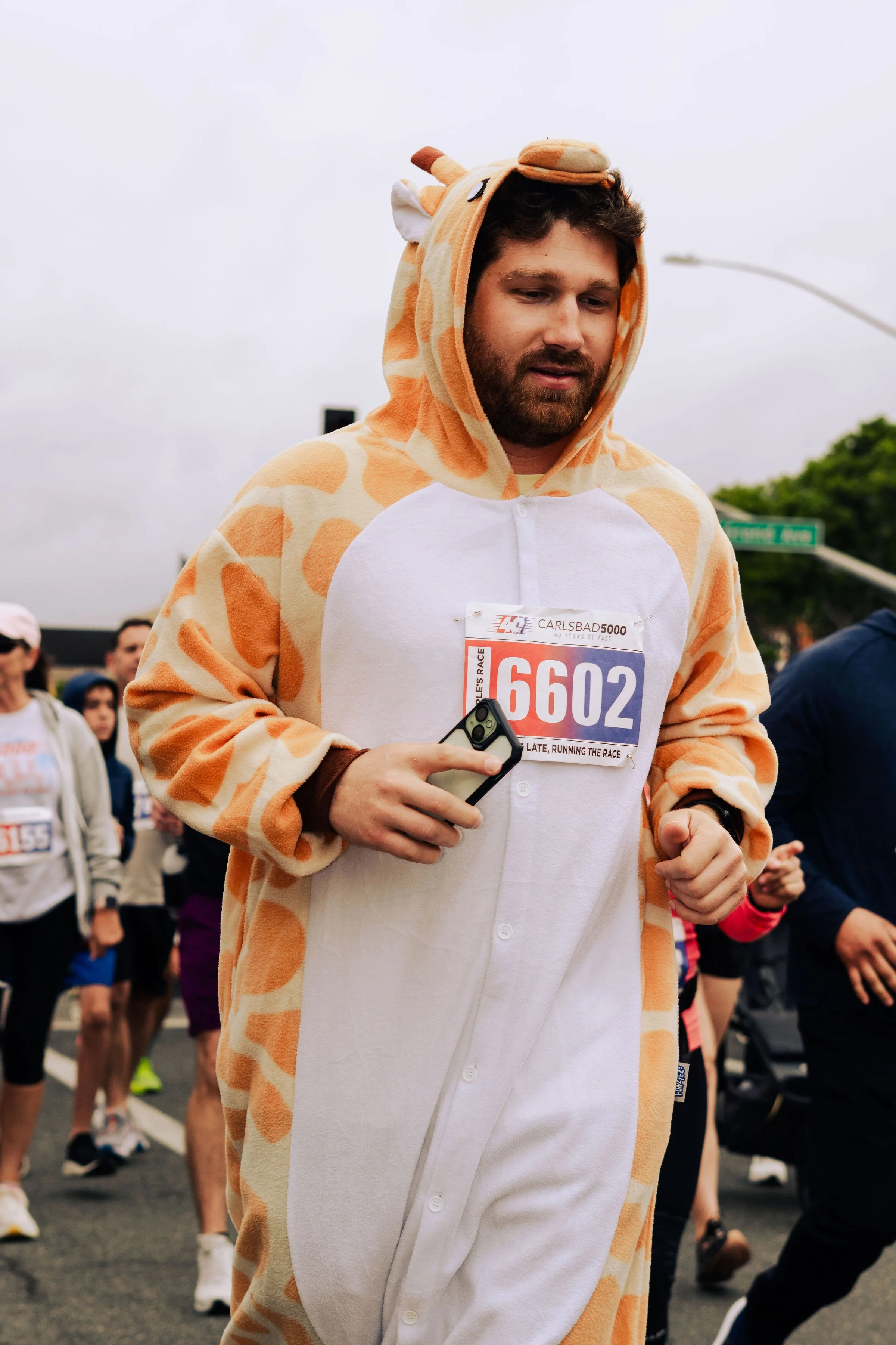 A man dressed in a giraffe costume running in a race during daytime with other runners around him.