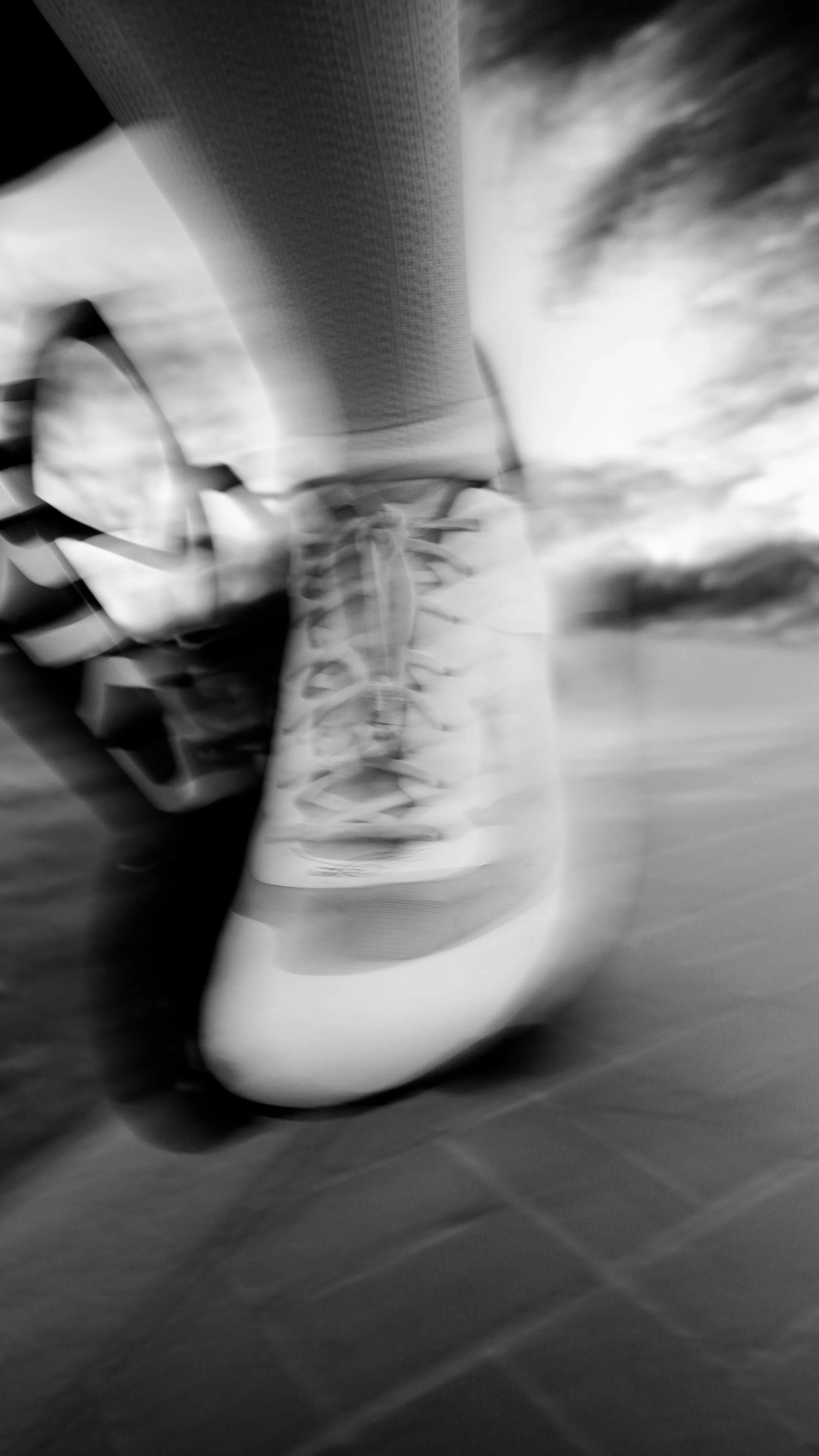 Close-up of a person running, focusing on their foot in a white athletic shoe and part of their leg on a tiled floor, with motion blur indicating movement.