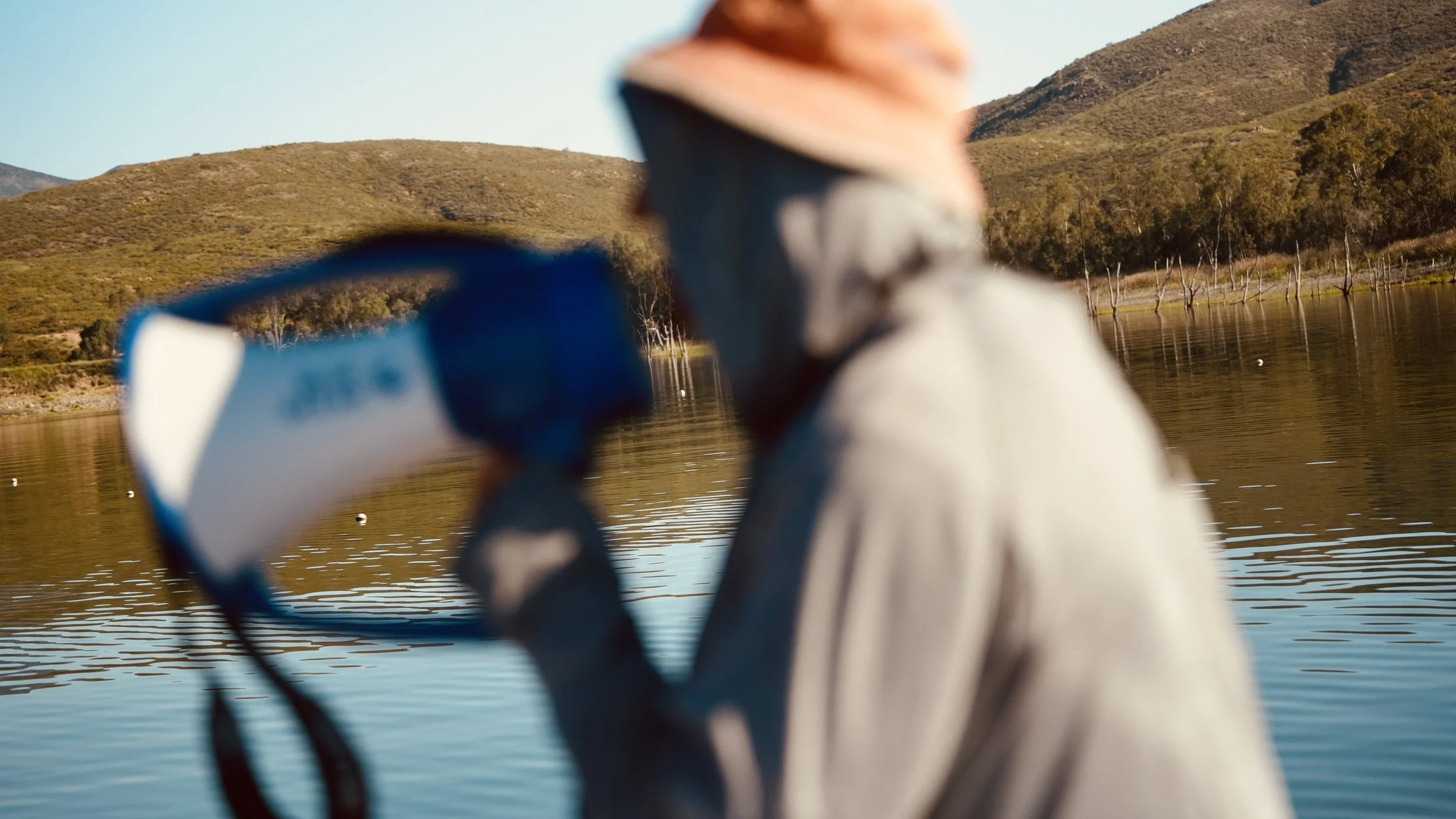Person wearing a hat and glasses kayaking on a calm river with mountains and trees in the background.