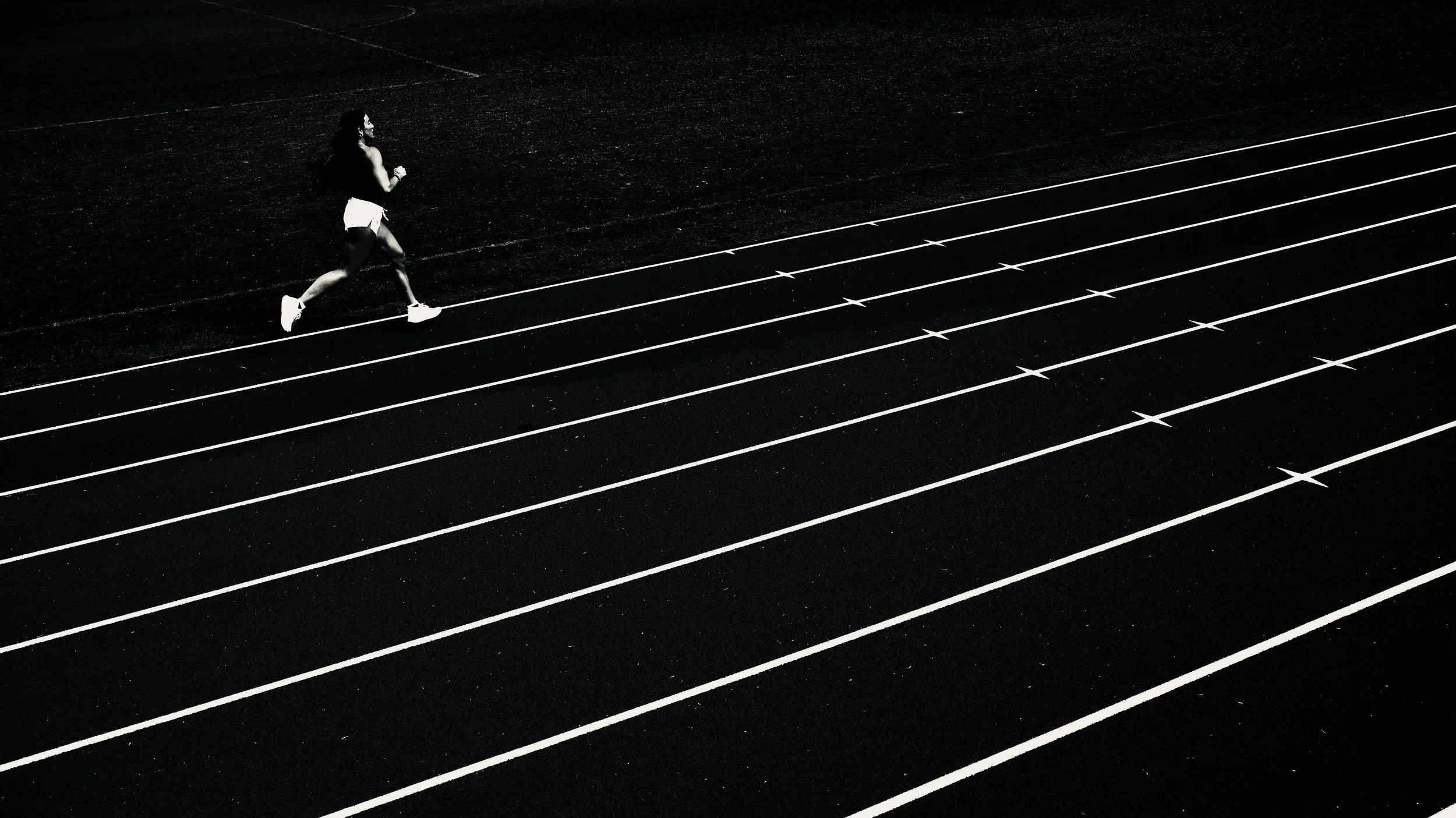 A person running on a black outdoor track with multiple white lanes, captured in black and white.