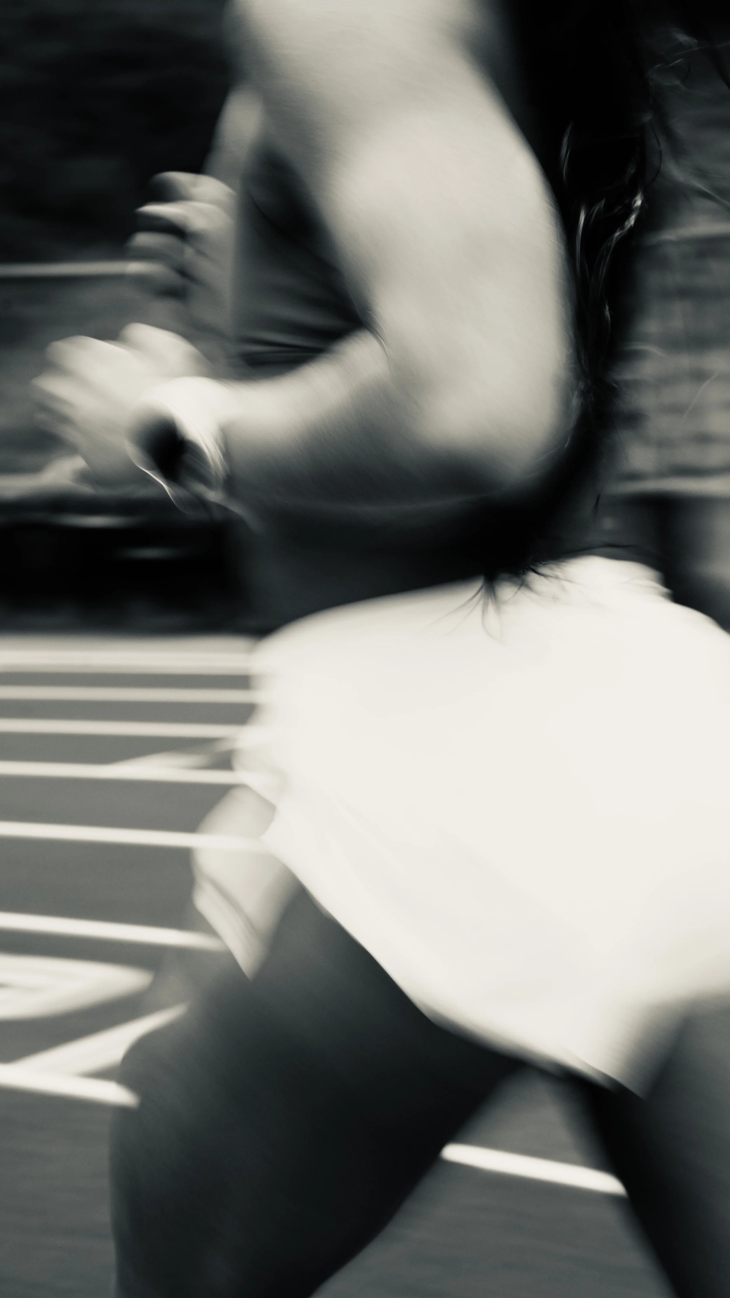 A person with long hair, wearing a white shirt, walking on a crosswalk, with motion blur.