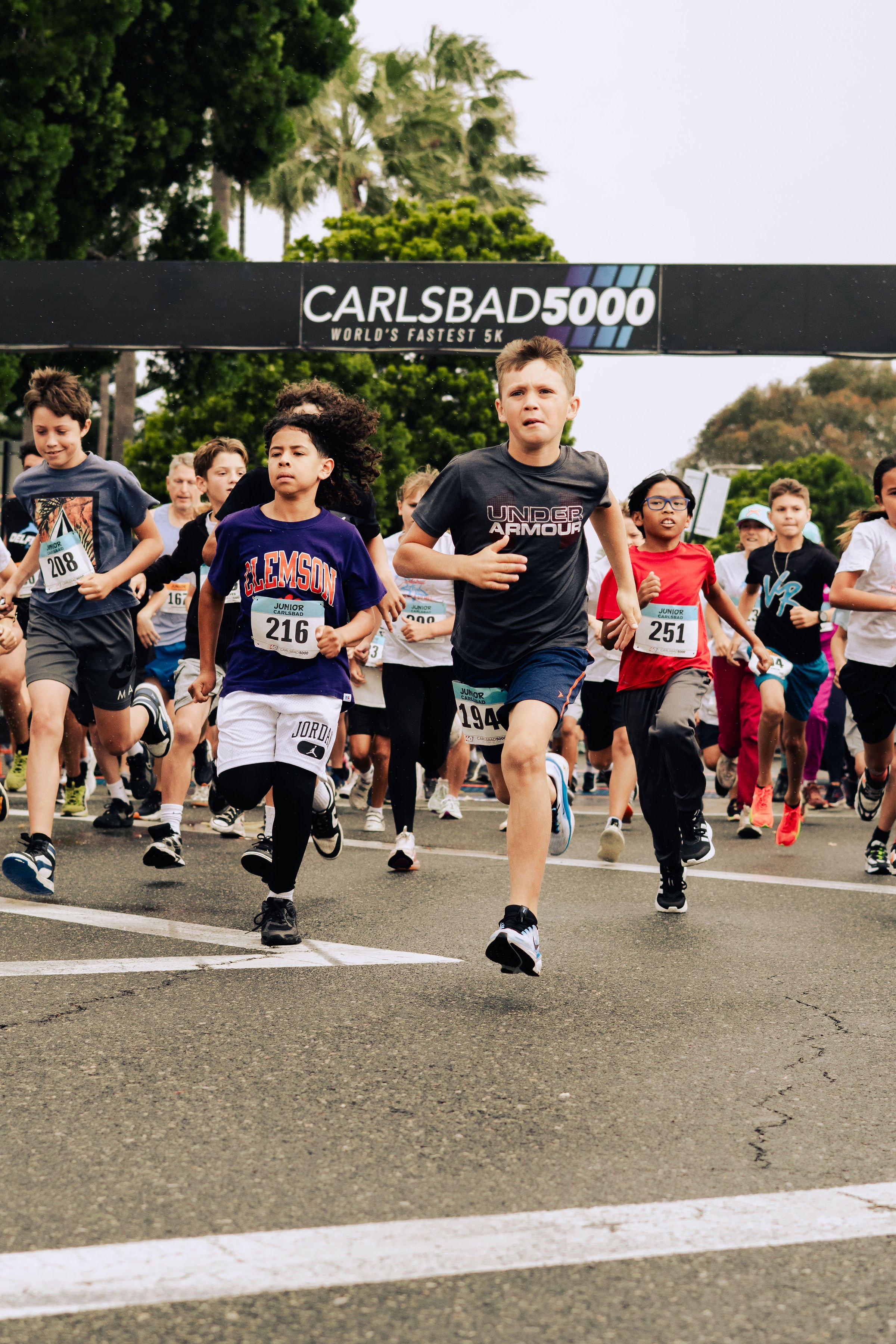 Children participating in a running race at a starting line with a sign that reads 'CARLSBAD 5000 WORLD'S FASTEST 5K'.