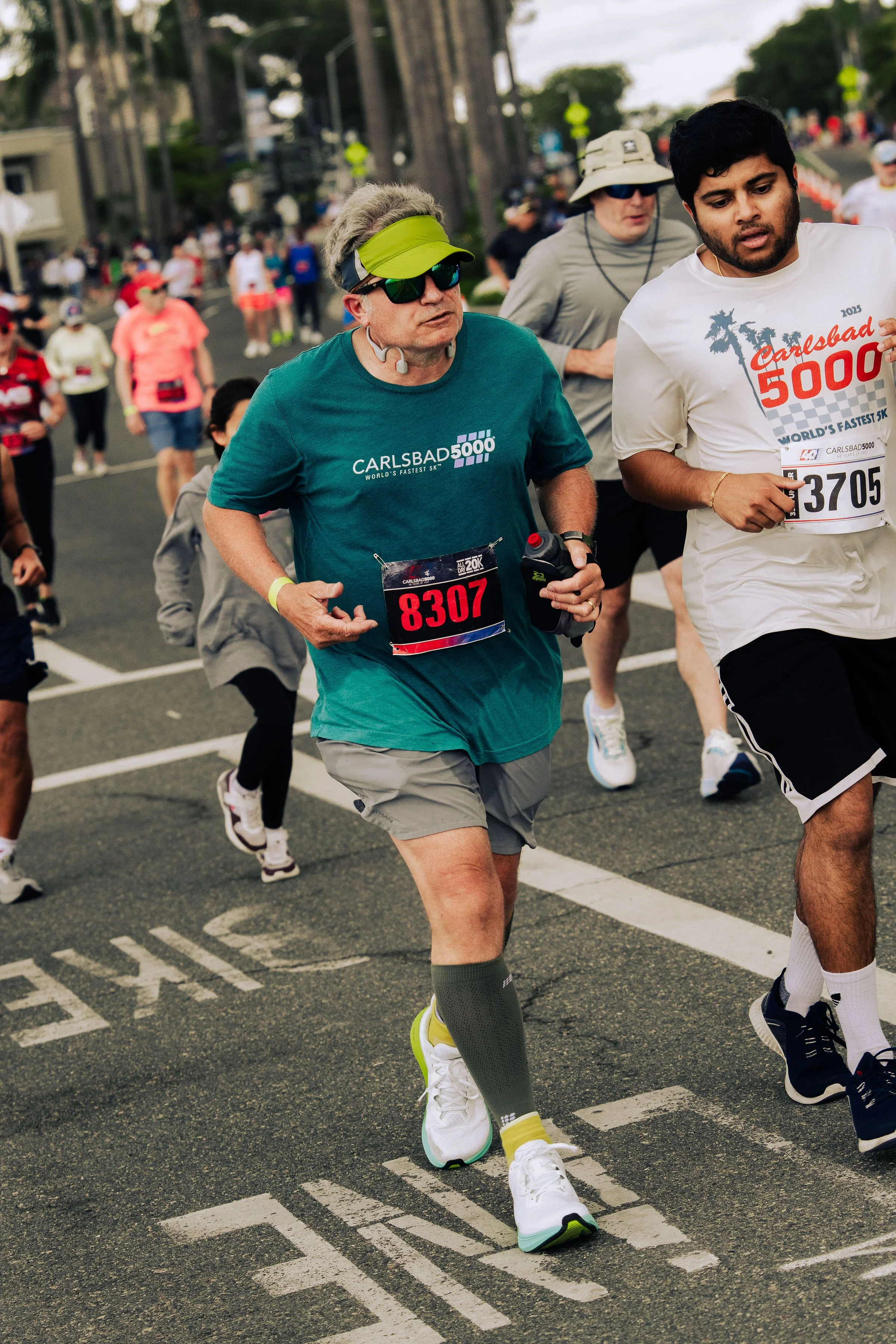 Group of runners participating in a race on the street, with some wearing race bibs and athletic gear.