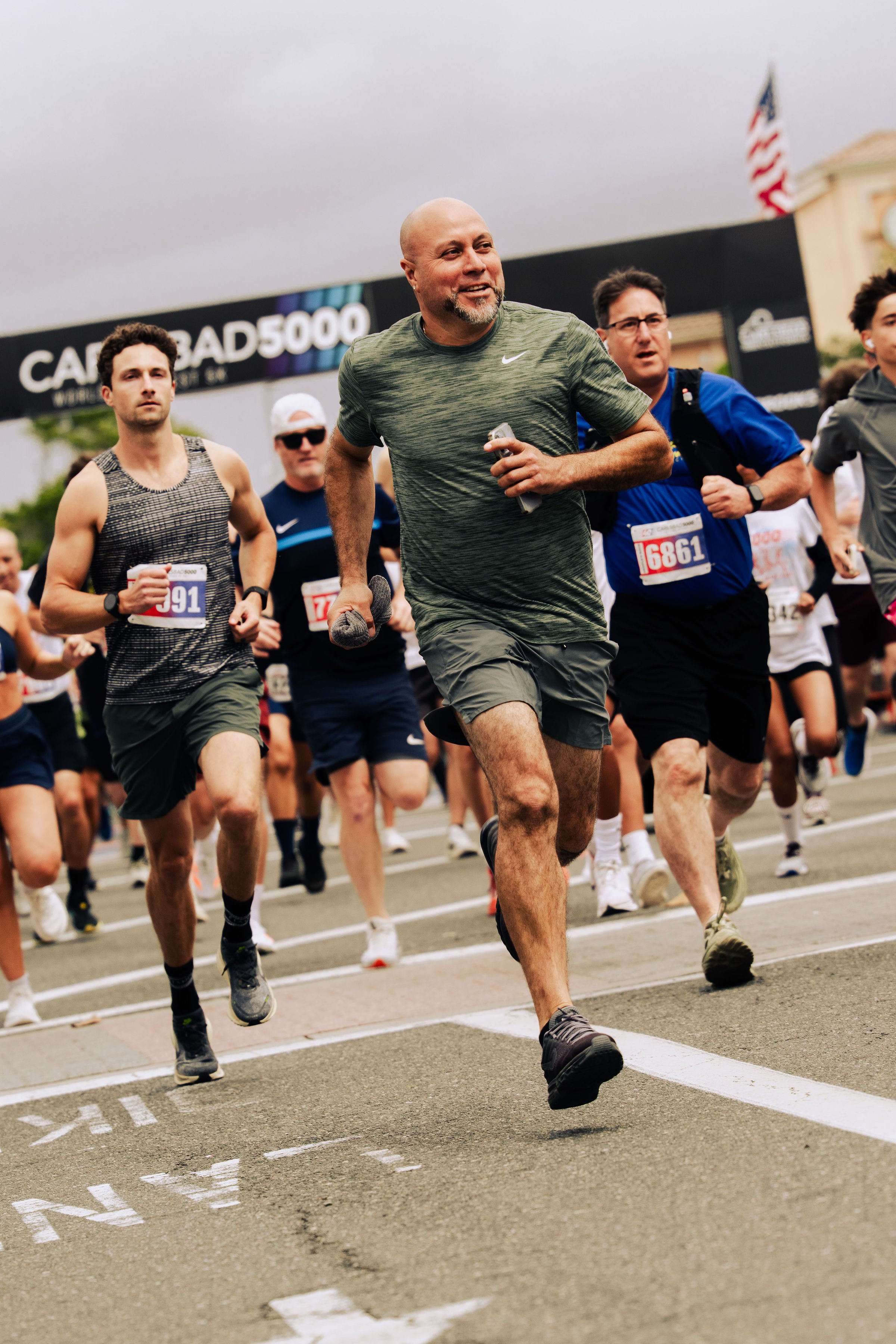 Runners participating in a marathon race, running on city streets with a large digital timer and American flag in the background.